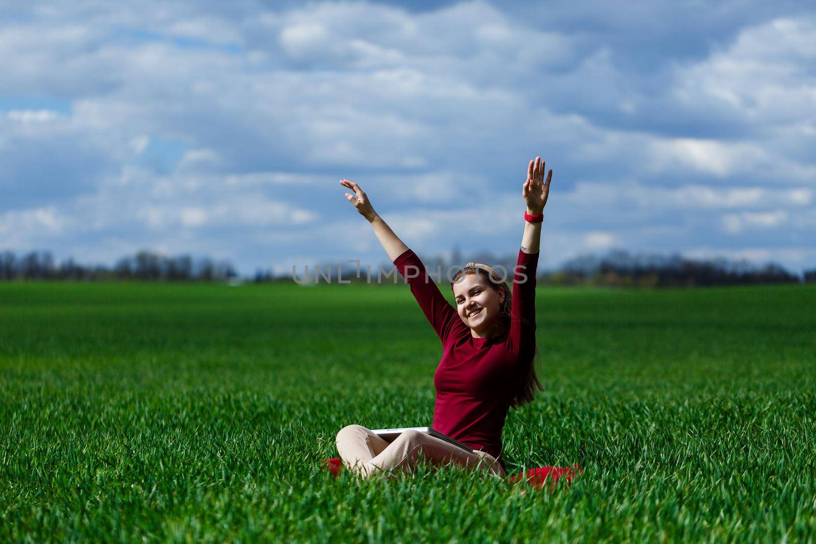 Young successful woman is sitting on green grass with a laptop in her hands. Rest after a good working day. Work on the nature. Student girl working in a secluded place. Workplace in nature