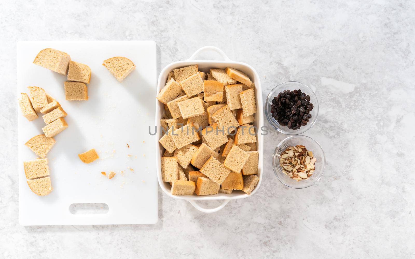 Flat lay. Baking bread pudding with raising and almond slivers in a white casserole dish.