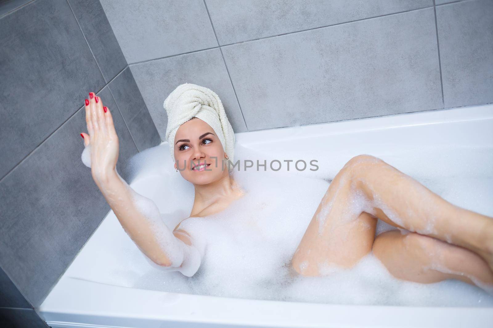 Girl woman with a white towel on her head lies in the bathroom in a white bath. Foam for around. Relax after a hard day. Spa relaxing treatment