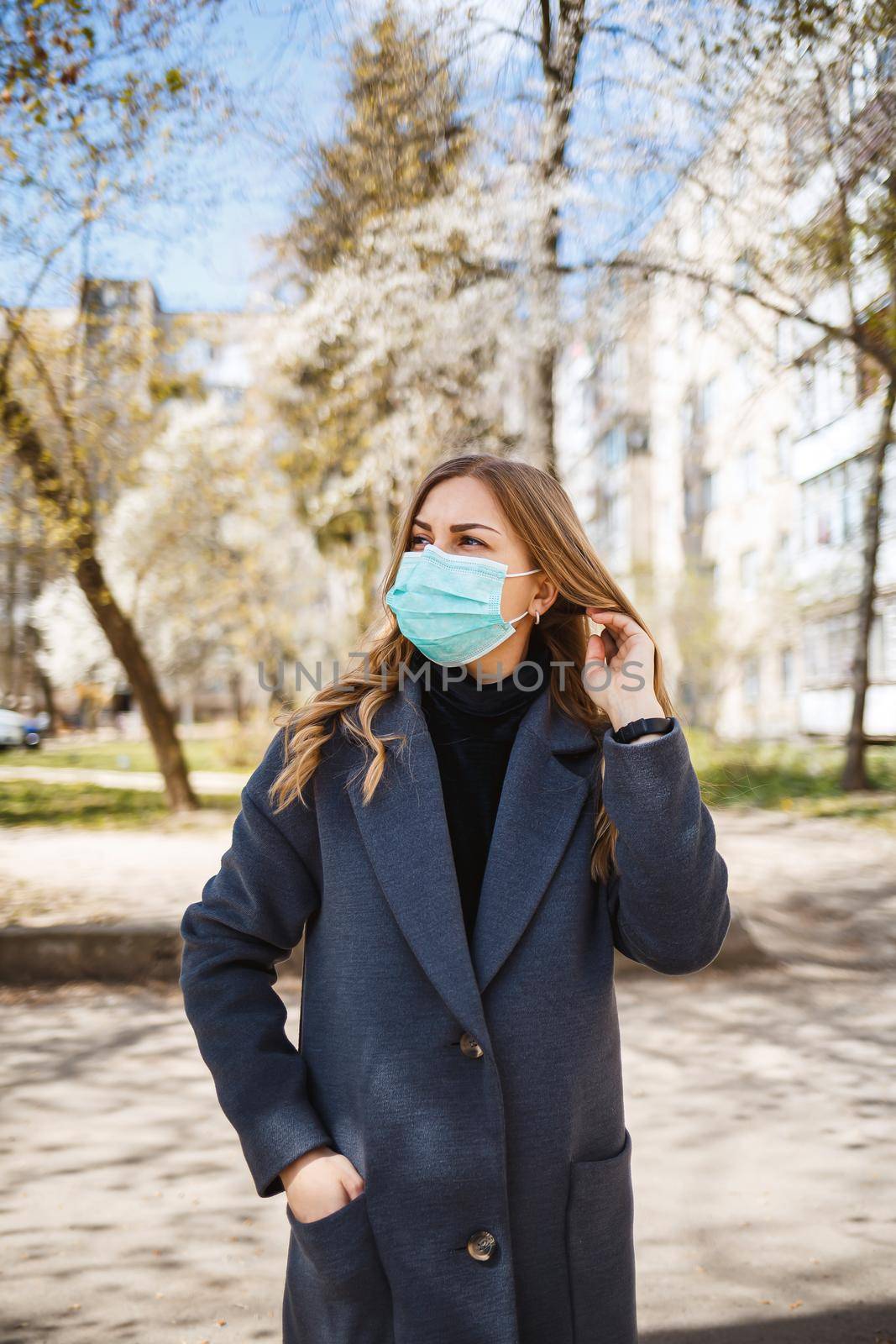 Girl, young woman in a protective sterile medical mask on her face, looking at the camera outdoors, in the spring garden. Air pollution, virus, pandemic coronavirus concept.