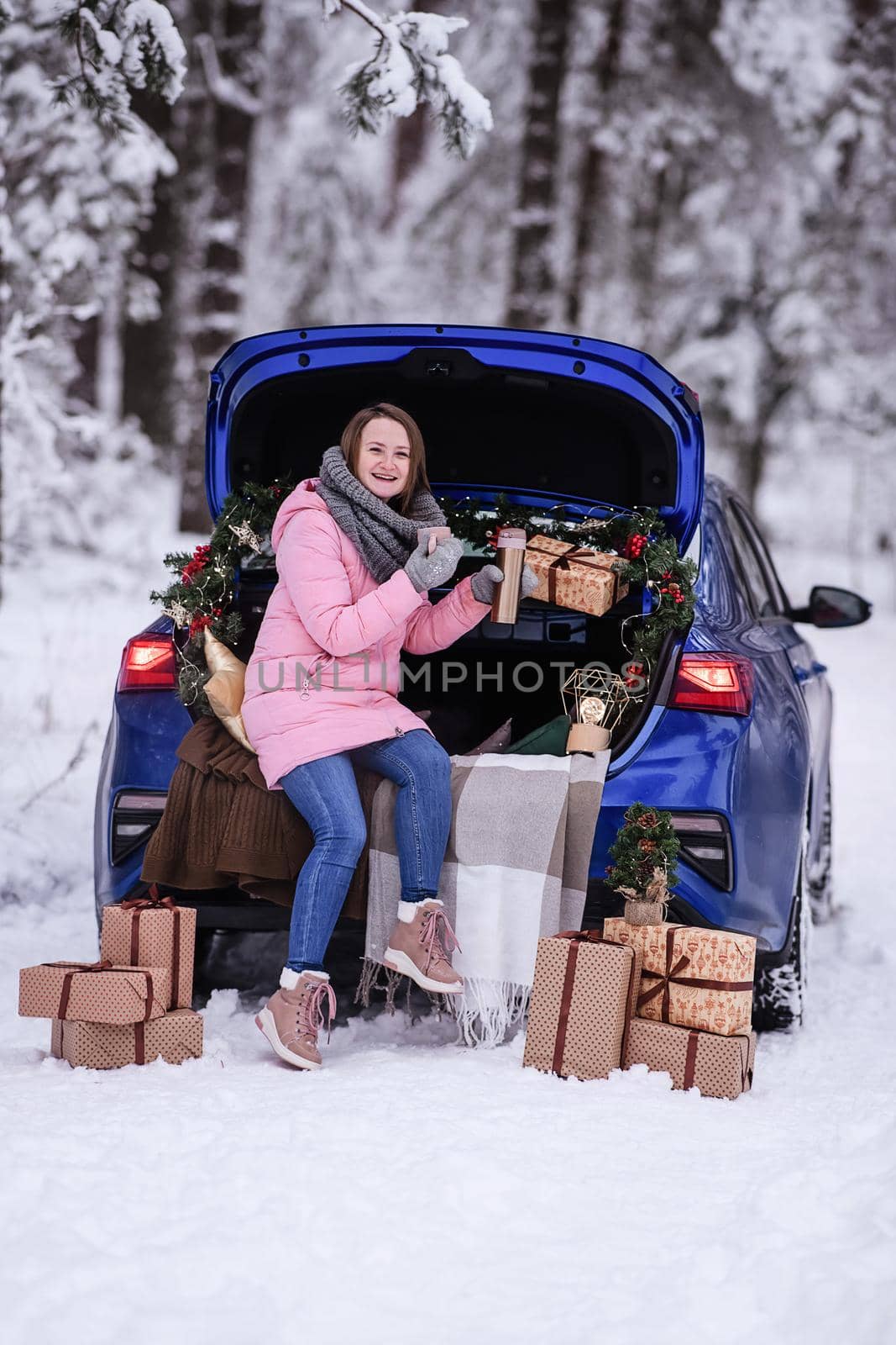 A woman in winter clothes drinks a hot drink sitting in a car decorated in a New Year's way. Traveling by car through the forest. A trip before Christmas by Annu1tochka