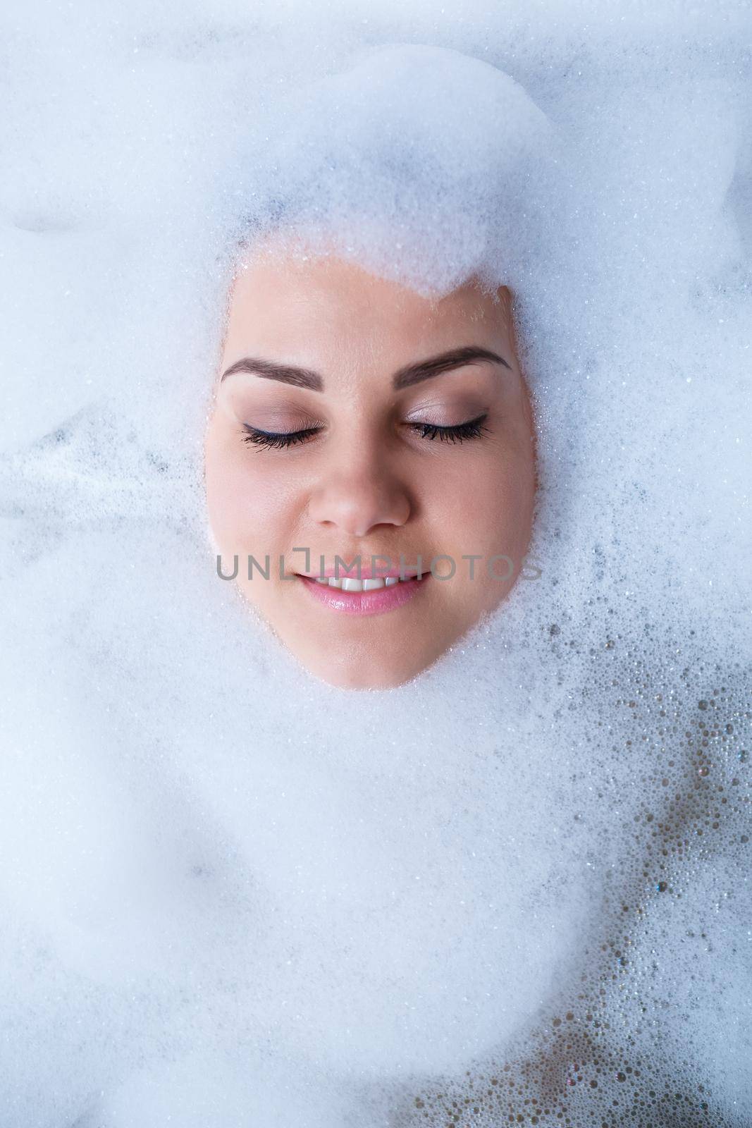 Closeup portrait of a girl in a bathtub and white foam around her face. Different emotions, grimaces, woman smile
