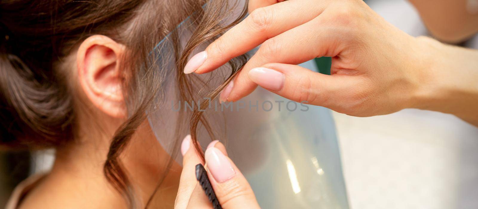 Close Up hairdresser stylist makes hairstyle for a young woman in a beauty salon