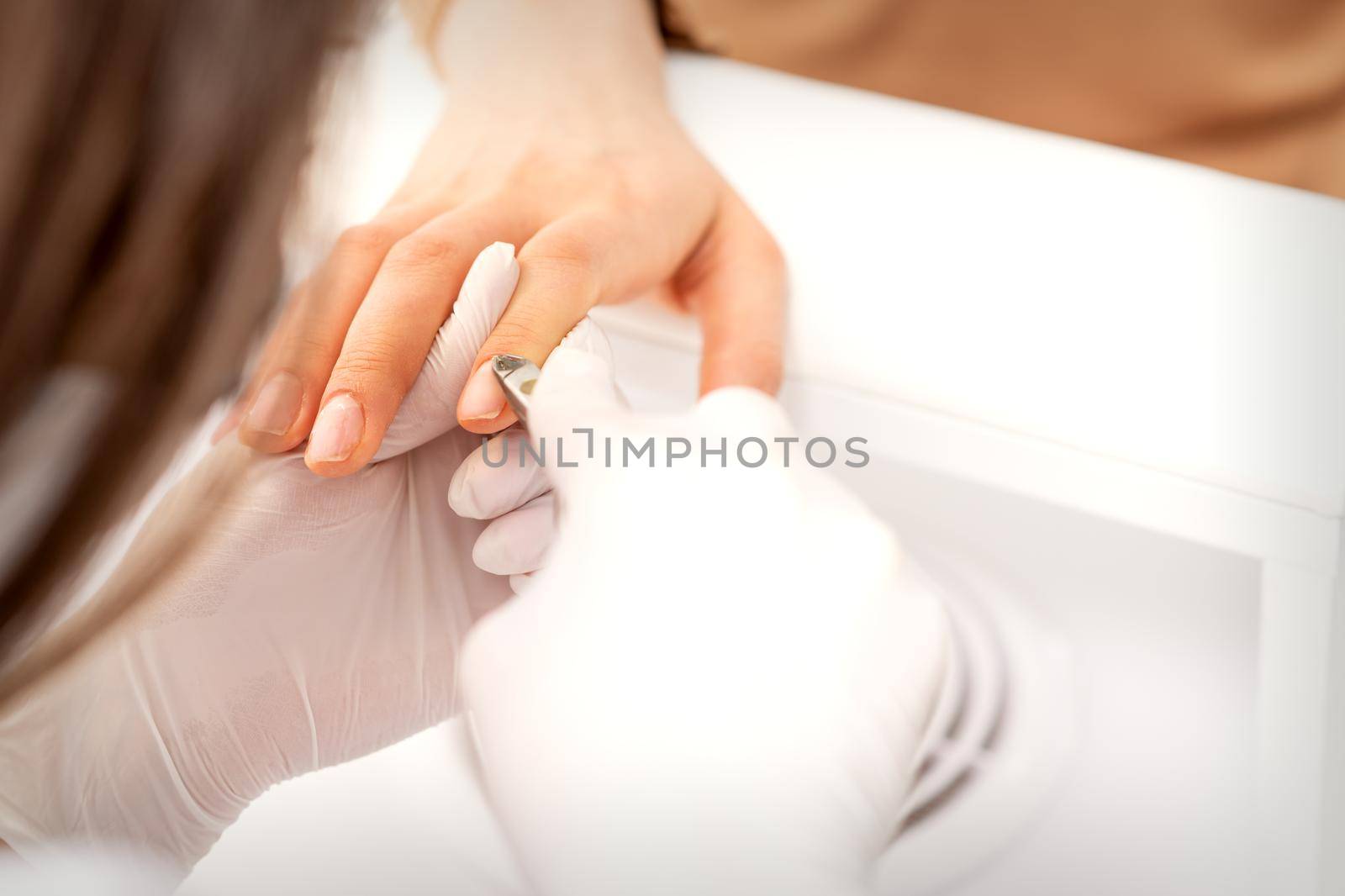 Manicure master uses manicure clippers removing cuticles on female nails in a beauty salon close up. by okskukuruza