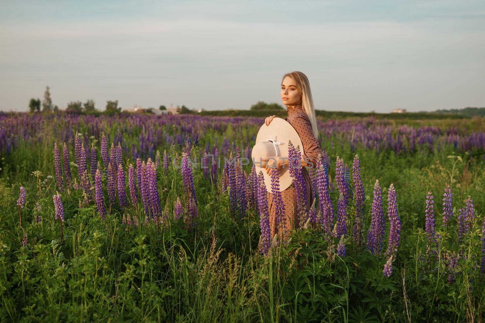 A beautiful woman in a straw hat walks in a field with purple flowers. A walk in nature in the lupin field by Annu1tochka