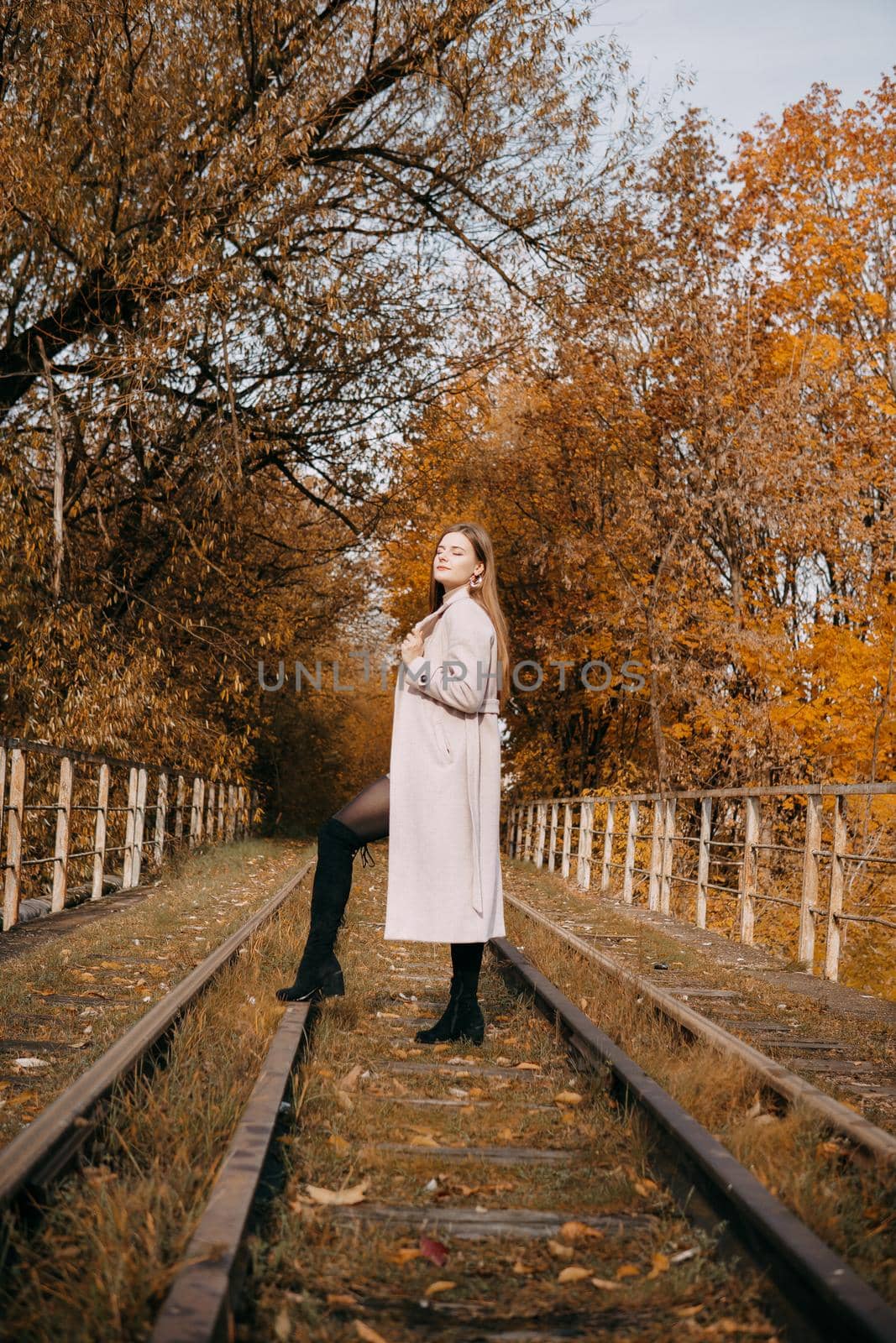 A beautiful long-haired woman walks through the autumn streets. Railway, autumn leaves, a woman in a light coat.