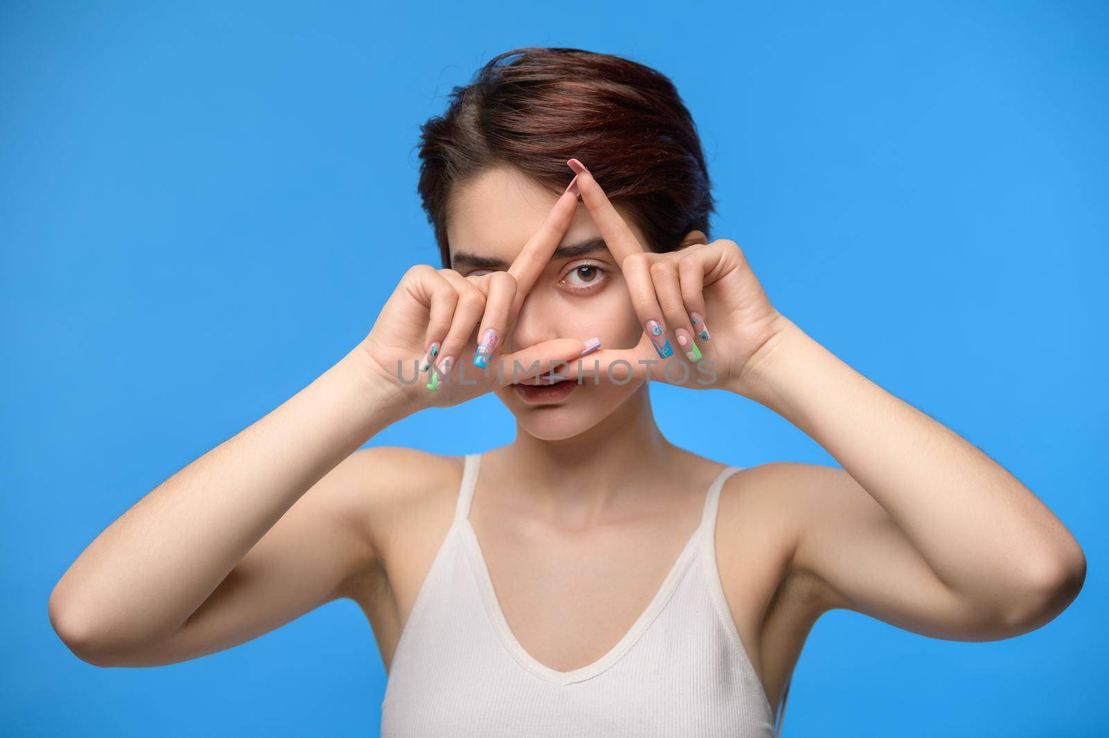 Young brunette woman with long nails with nailart looking through triangle finger frame