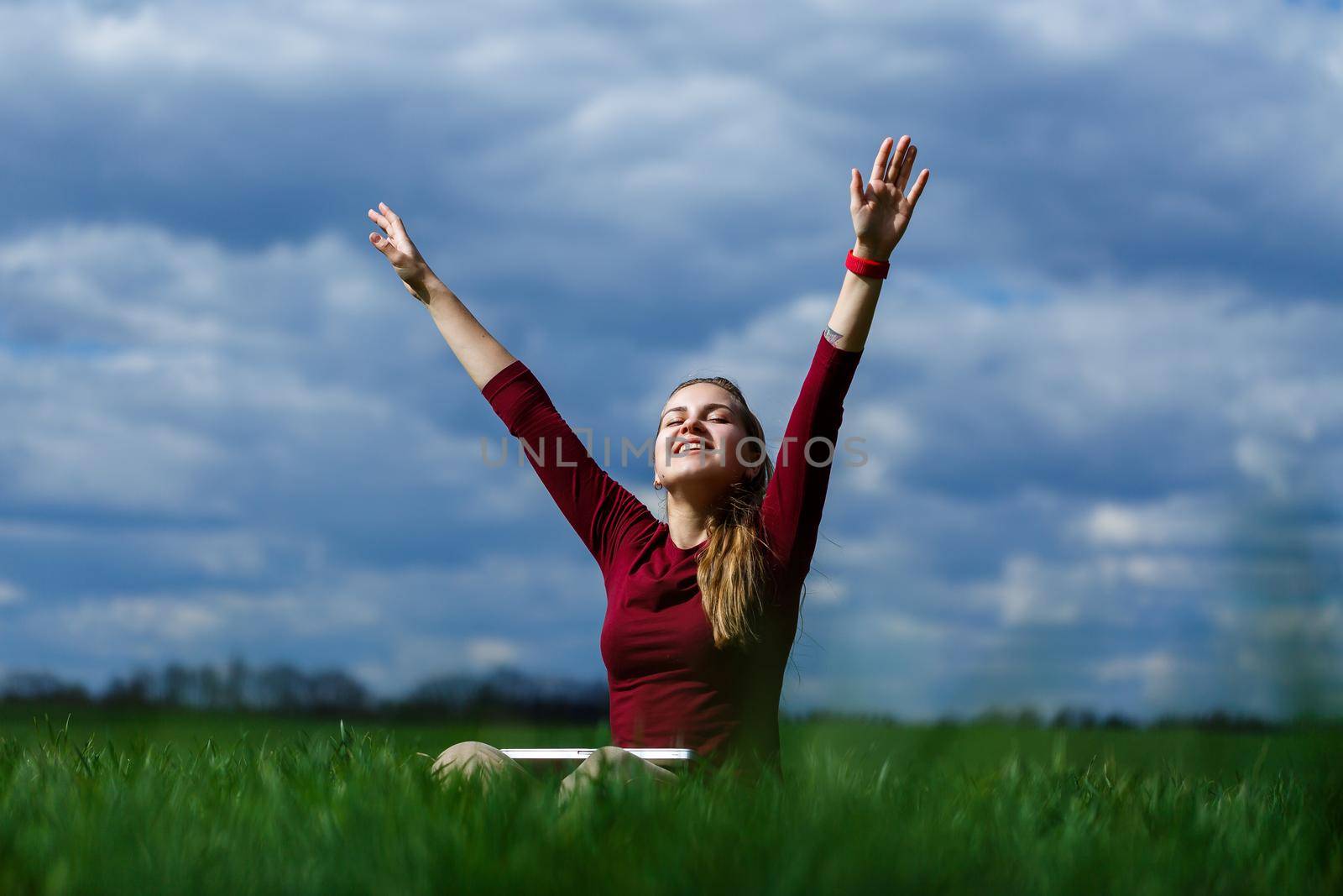 Young successful woman is sitting on green grass with a laptop in her hands. Rest after a good working day. Work on the nature. Student girl working in a secluded place. Workplace in nature