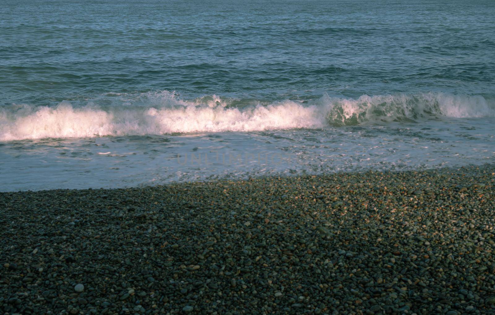 Sea waves wash over a pebble beach made of natural rounded gravel.