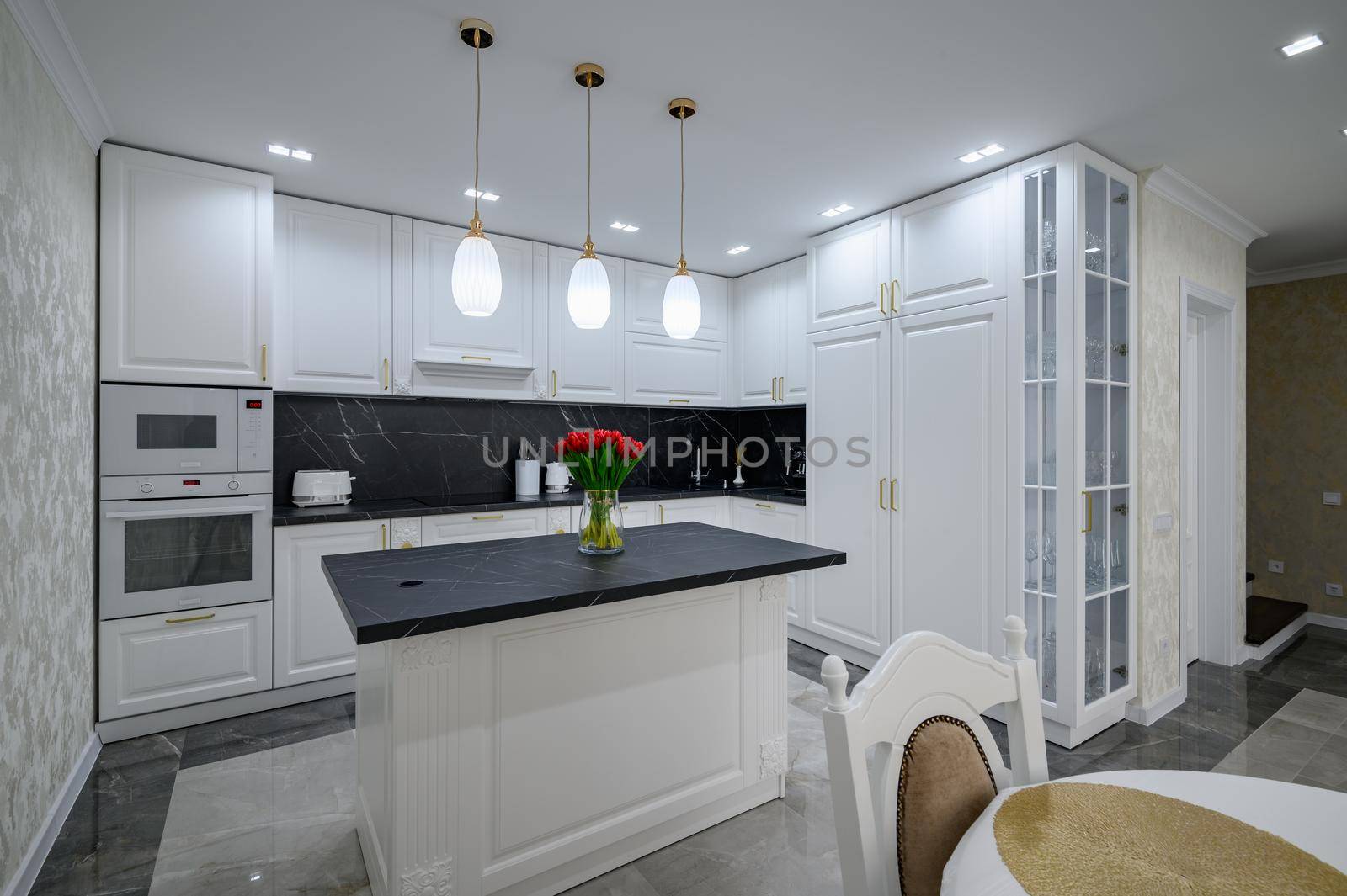 Luxurious white large modern domestic kitchen with black marble worktop and serverd dining table