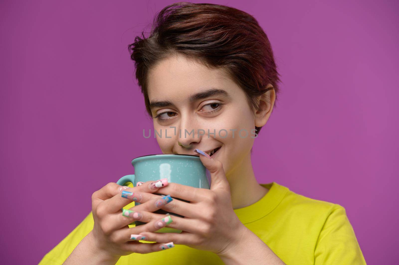 A barely awake pretty brunette enjoys her morning tea or coffee, cheering herself up, studio shot at magenta background