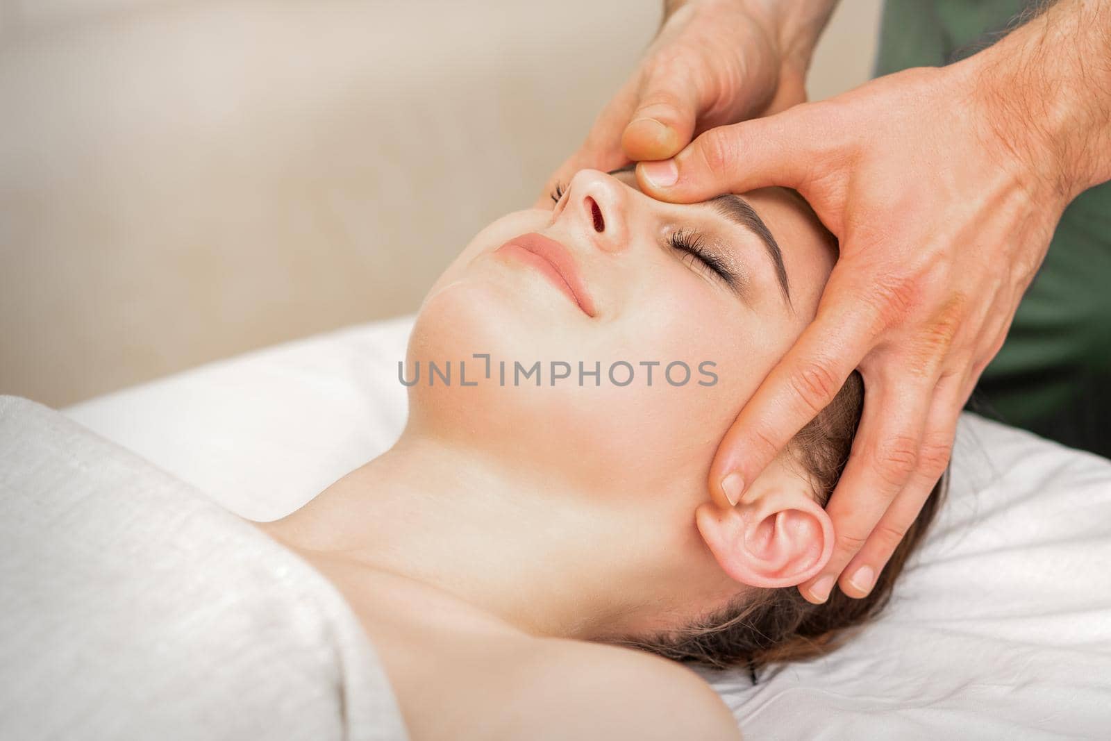 Pretty young caucasian woman receiving a head massage by a male massage therapist in a beauty salon. by okskukuruza
