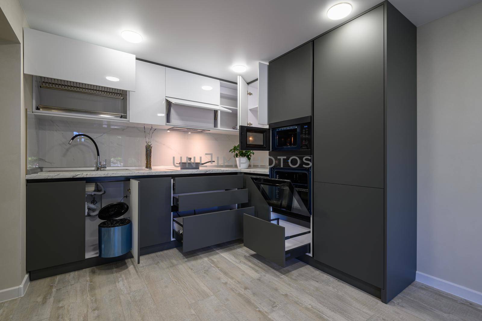 Showcase interior of modern simple dark grey and white kitchen, drawers retracted, doors open
