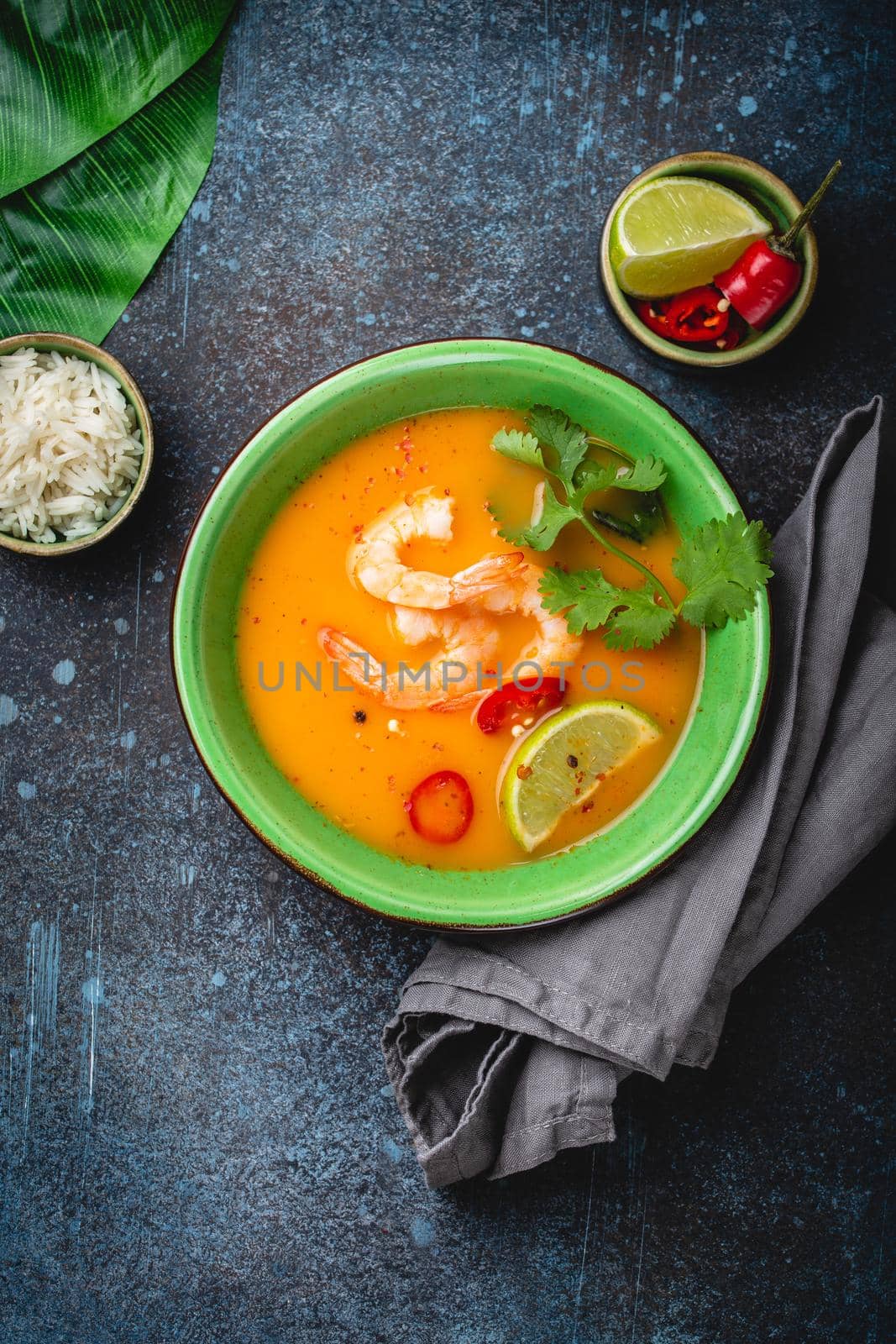 Traditional healthy Thai soup tom yum with shrimps, lime, coriander in bowl on rustic background with white rice, overhead shot. Authentic Thai food concept with copy space .