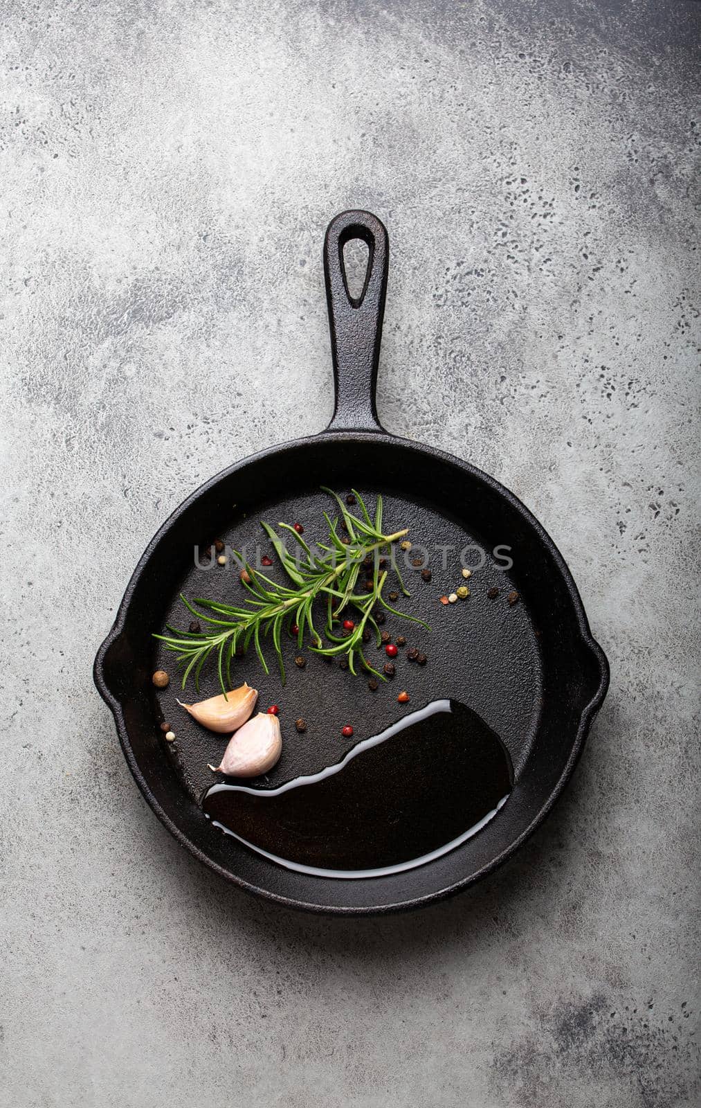 Black cast iron frying pan with rosemary, garlic, pepper, oil by its_al_dente