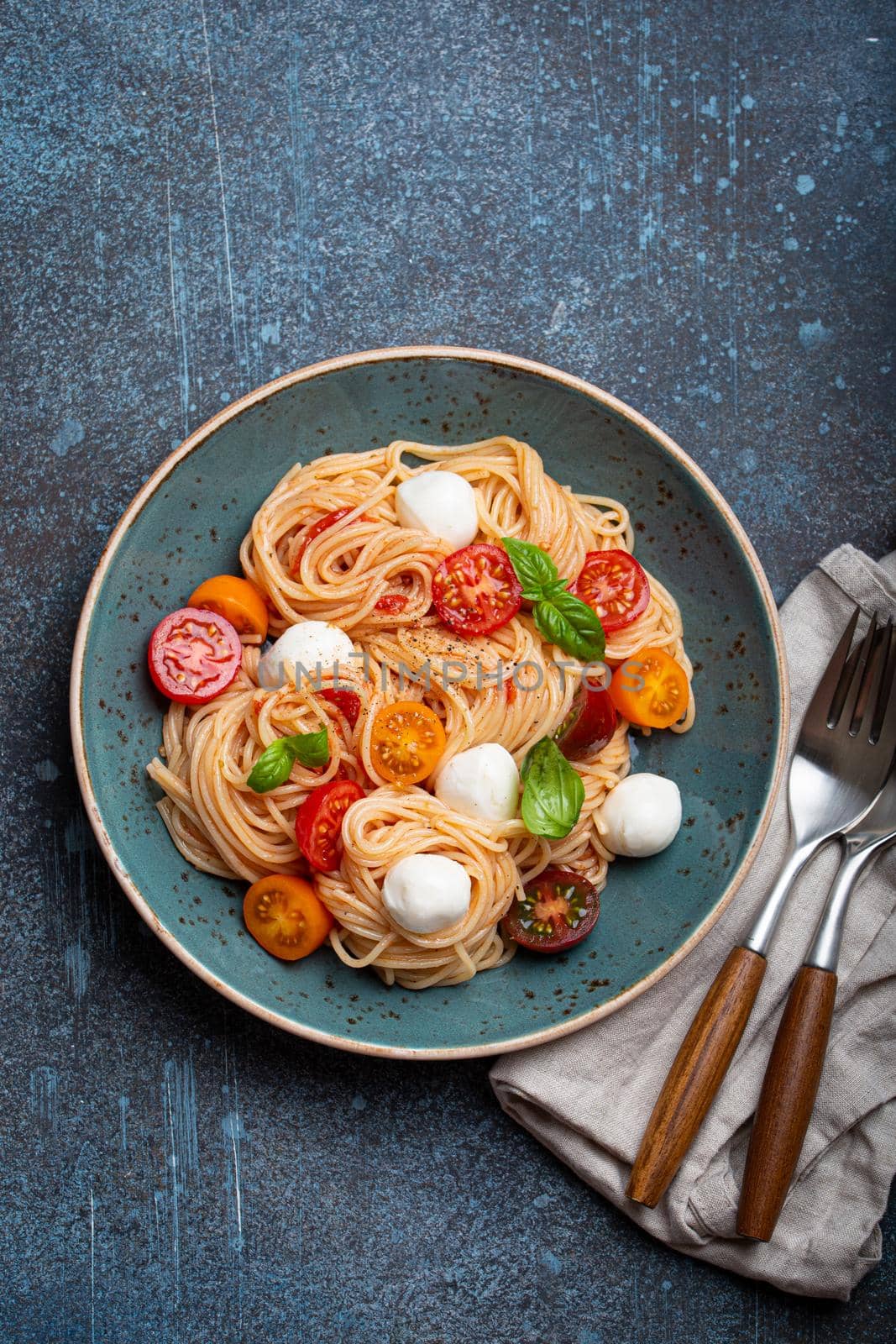 Delicious spaghetti with mozzarella, colourful cherry tomatoes, fresh basil on ceramic plate on rustic stone background top view. Italian healthy tasty food pasta for dinner or lunch