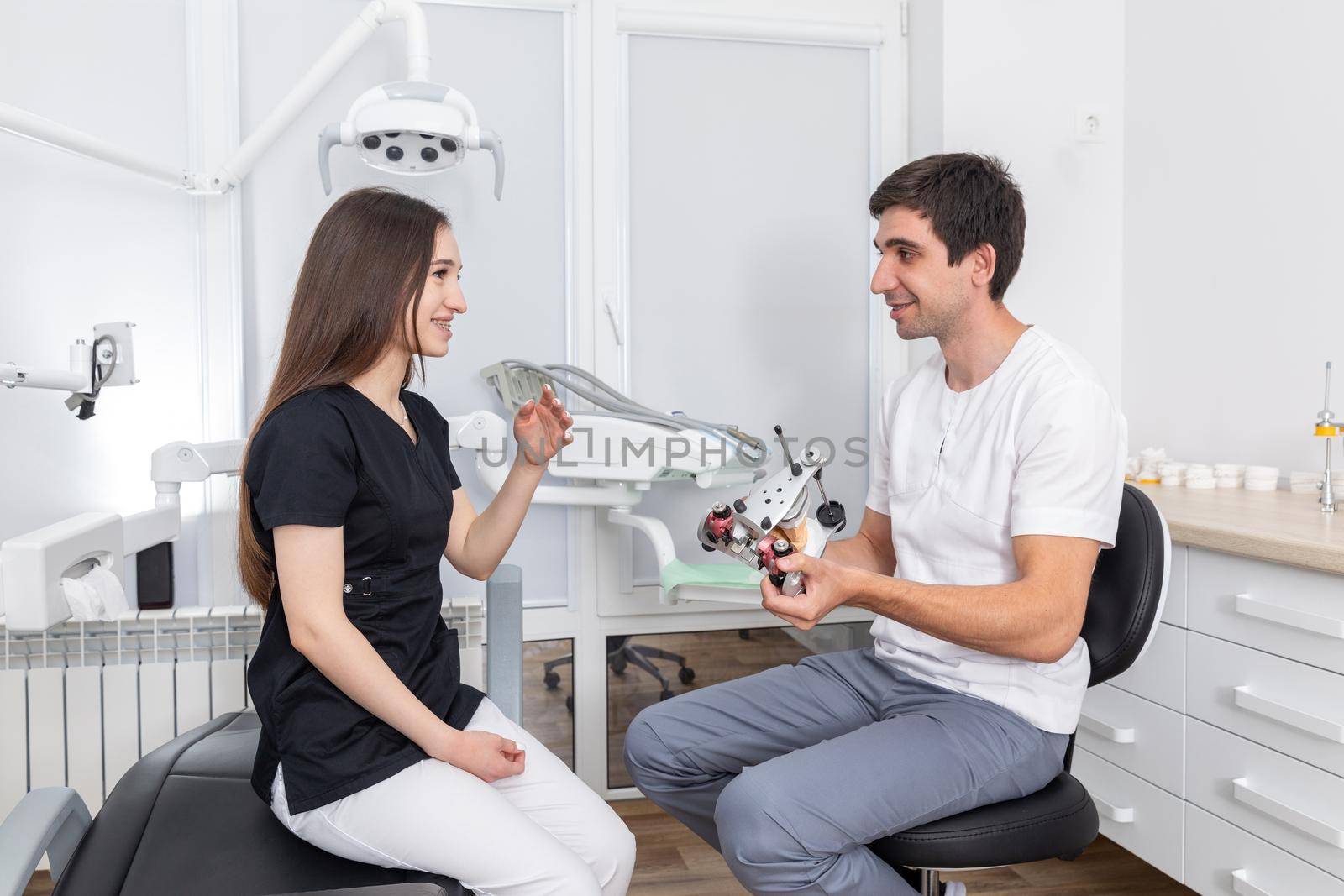 Dentist holding dental articulator with dental gypsum prosthesis model showing it to a patient by Mariakray