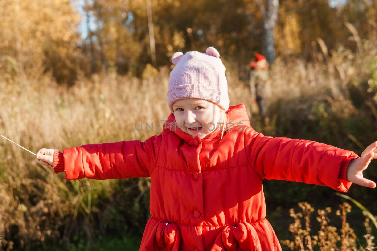 A little girl in a red coat walks in nature in an autumn grove. The season is autumn.