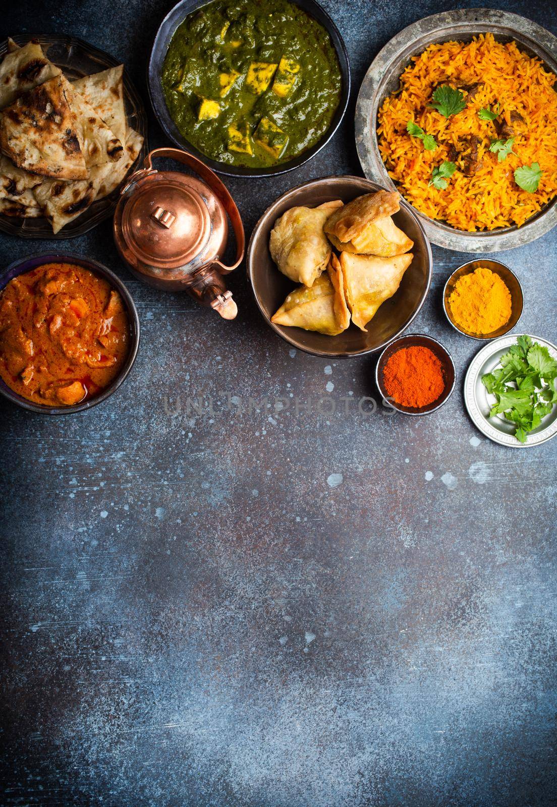 Overhead of Indian traditional dishes and appetizers: chicken curry, pilaf, naan bread, samosas, paneer, chutney on rustic background. Table with choice of food of Indian cuisine, space for text