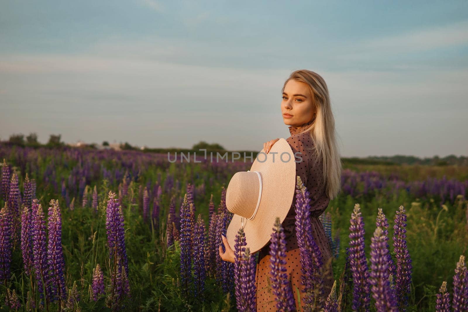 A beautiful woman in a straw hat walks in a field with purple flowers. A walk in nature in the lupin field by Annu1tochka