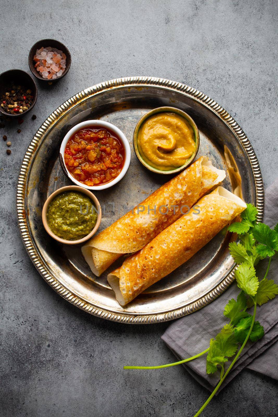 Traditional Indian rice pancakes Dosa with different dips chutney and seasonings on rustic metal plate on stone background table. Quick meal or vegetarian snack of South India, top view