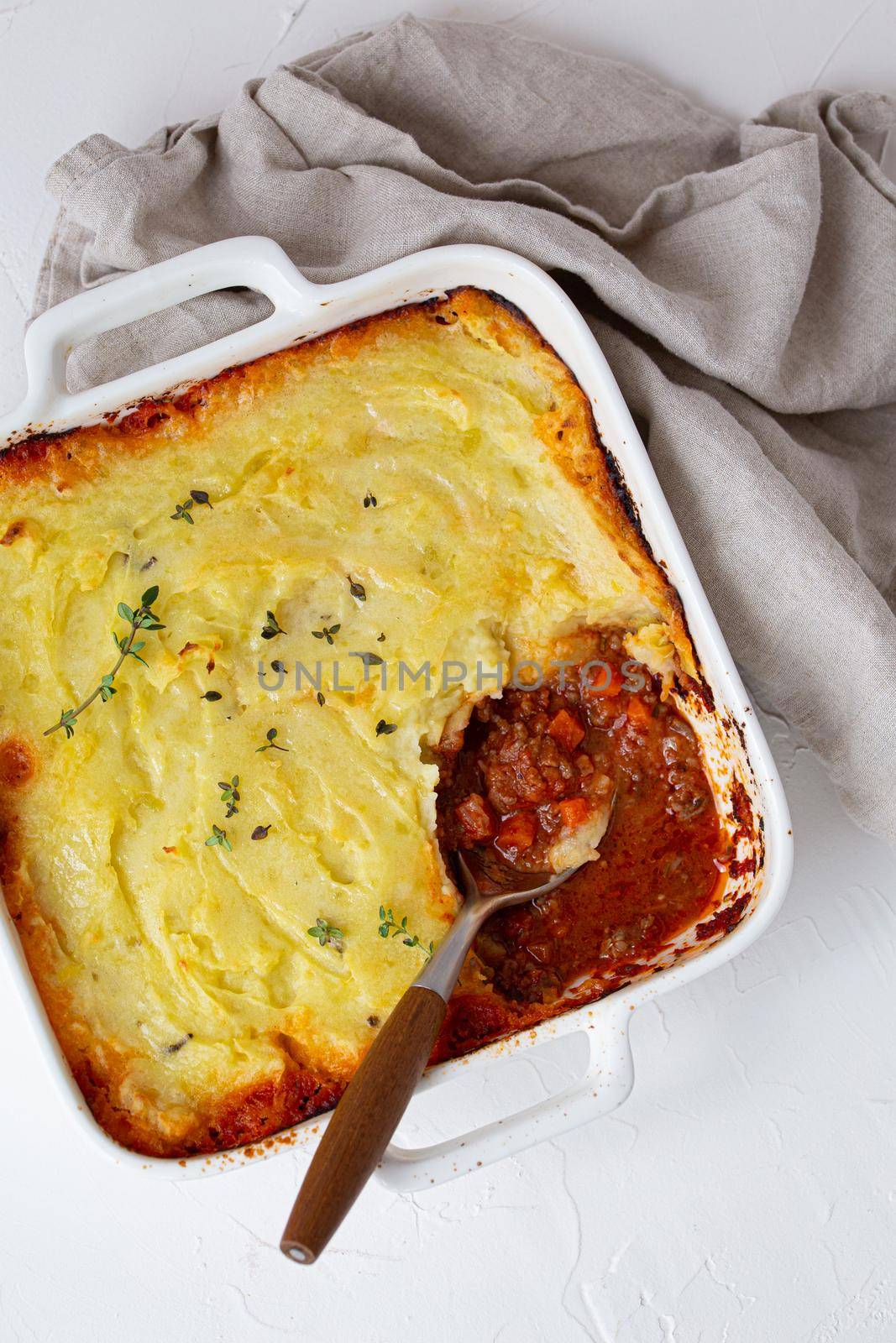 Traditional dish of British cuisine Shepherd's pie casserole with minced meat and mashed potatoes in ceramic baking dish on white rustic table with spoon from above