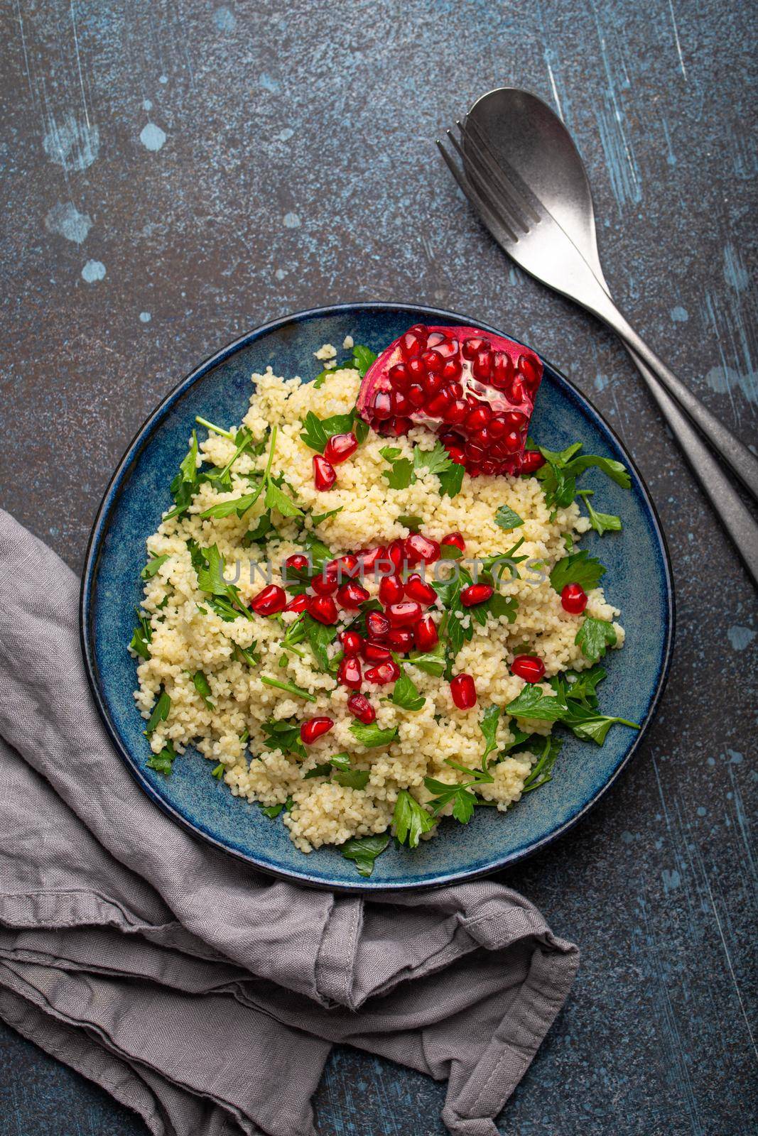 Bright colourful couscous or bulgur salad with pomegranate seeds Tabbouleh in rustic blue ceramic bowl top view on concrete background, traditional middle eastern or arab dish.