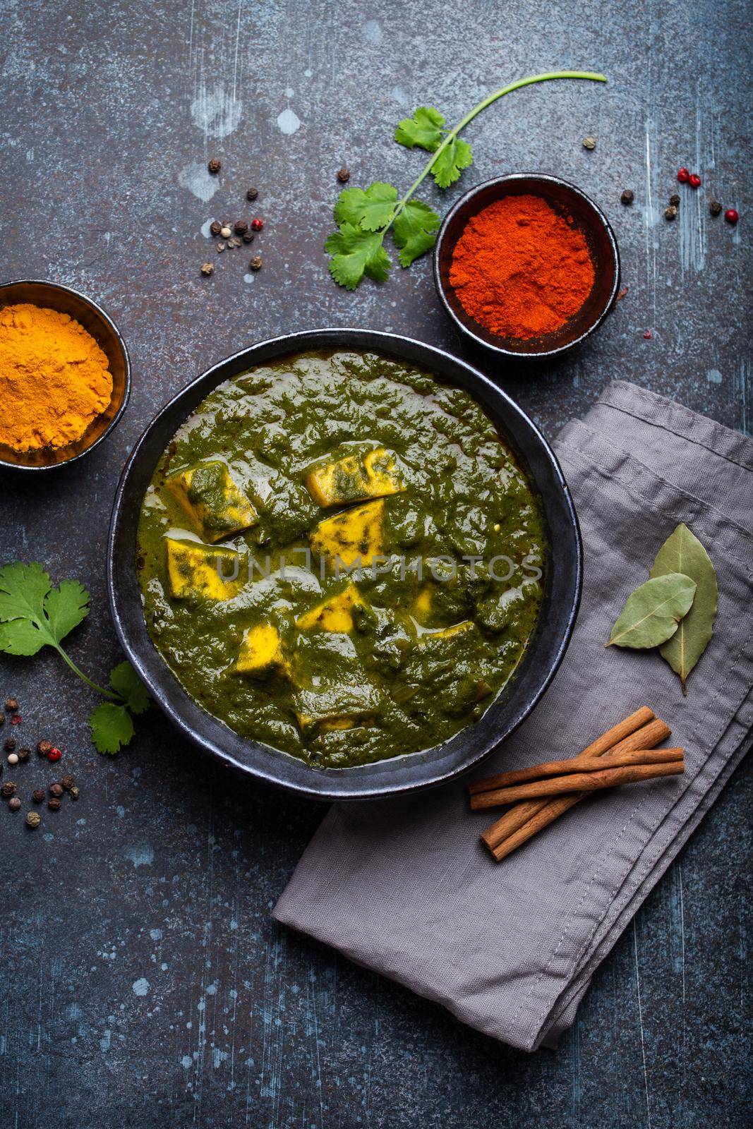 Palak paneer, traditional vegetarian Indian dish with cheese paneer, pureed spinach and spices. Indian green paneer curry in rustic ceramic bowl on concrete background, top view