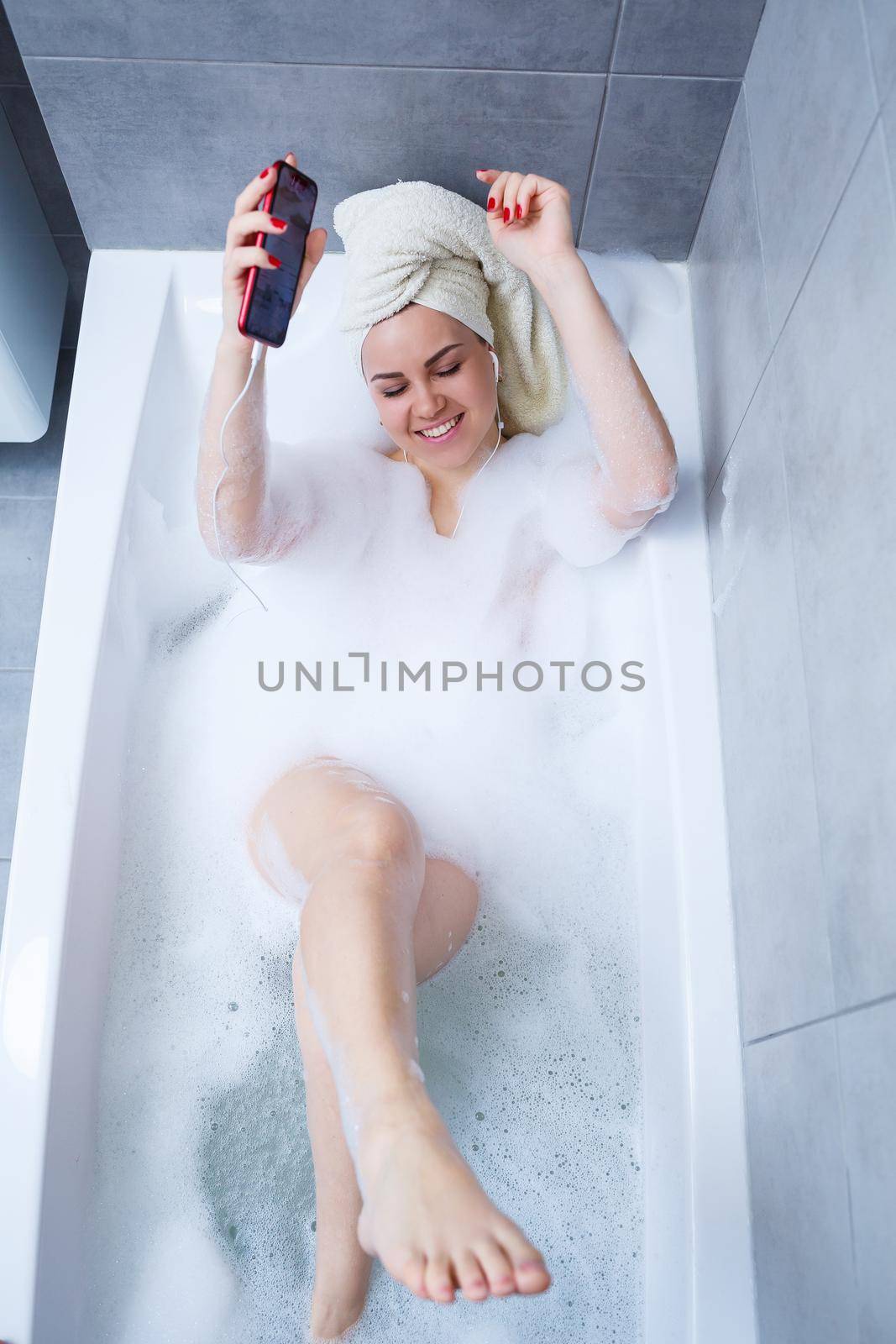 Beautiful young woman listens to music with headphones and sings while taking a bath at home. Relax after a hard day. Relaxing spa treatment.