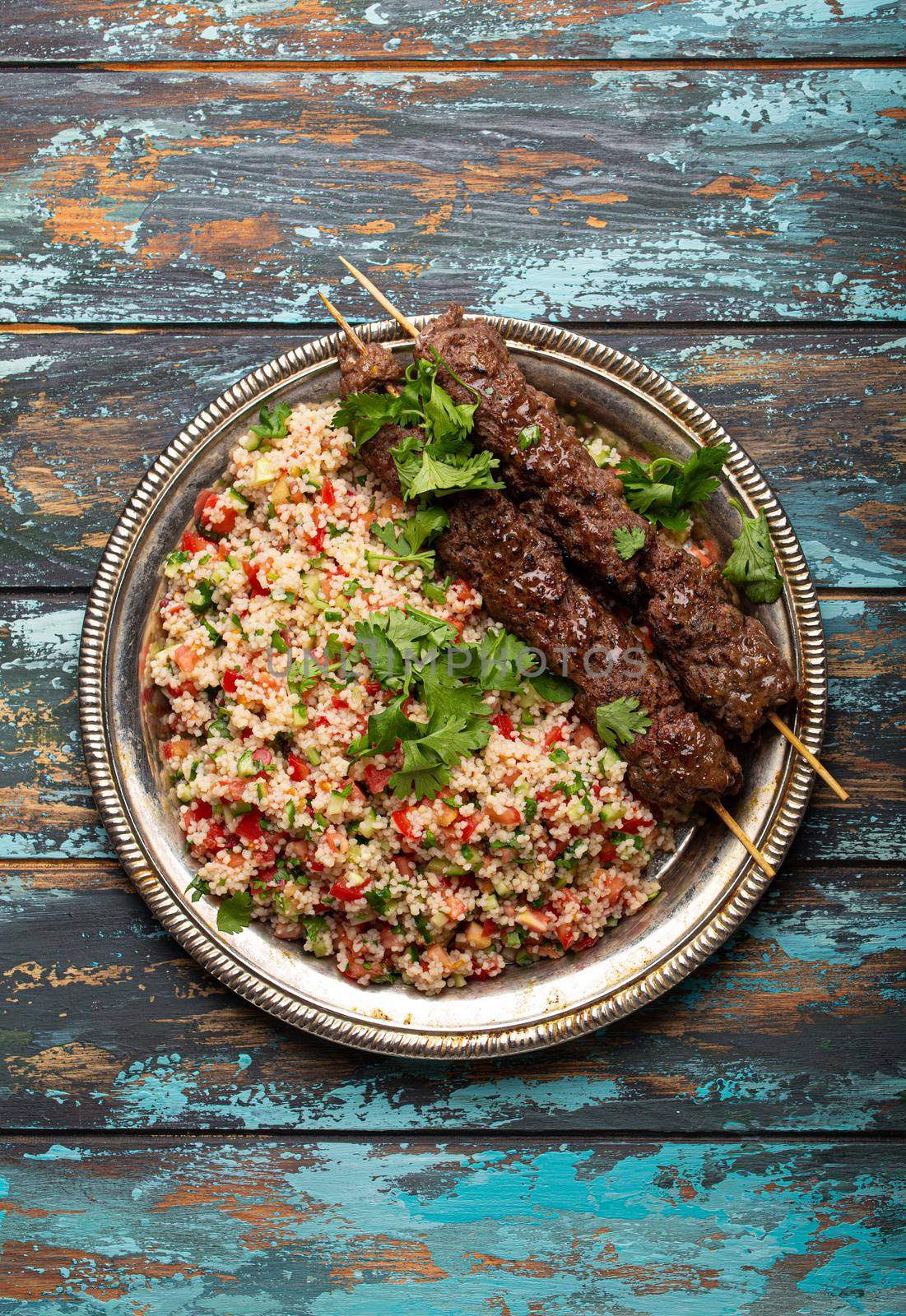 Middle eastern Turkish dinner with meat kebab and couscous salad tabbouleh on rustic metal plate on wooden background top view, traditional Arab meal