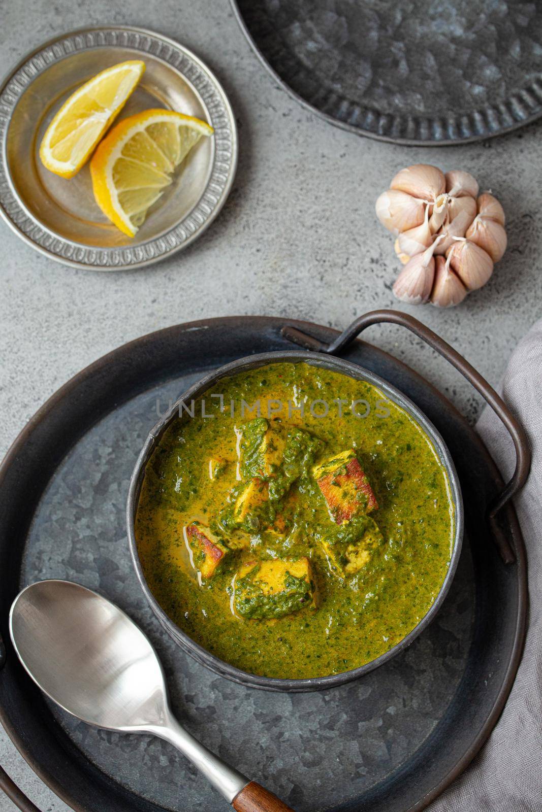 Traditional Indian Punjabi food Palak Paneer with spinach and cheese in vintage metal bowl with spoon on rustic grey concrete background table from above