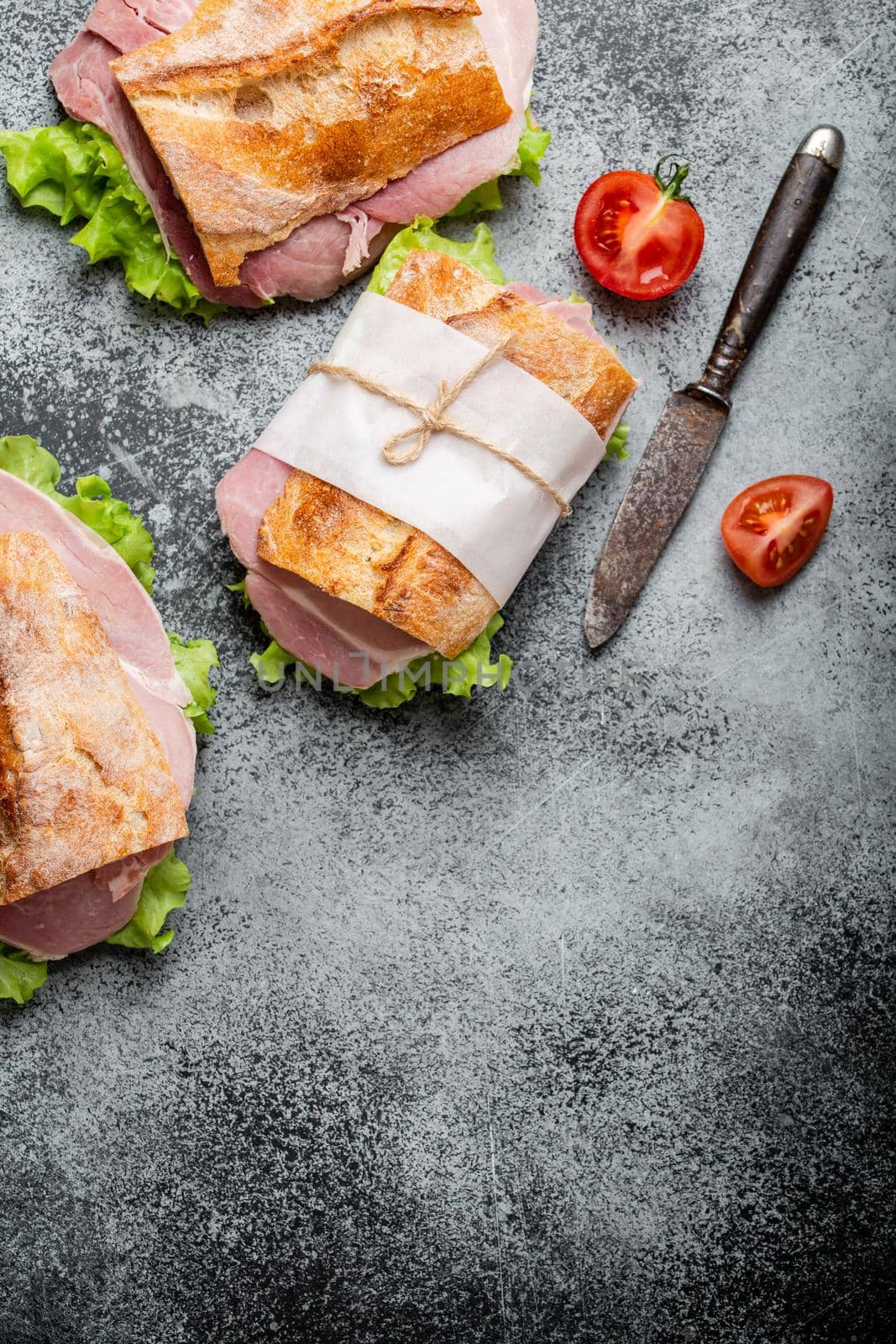Fresh ciabatta sandwiches with ham, cheese, lettuce, tomatoes on stone concrete background, close-up, top view. Making healthy sandwiches for snack or lunch concept