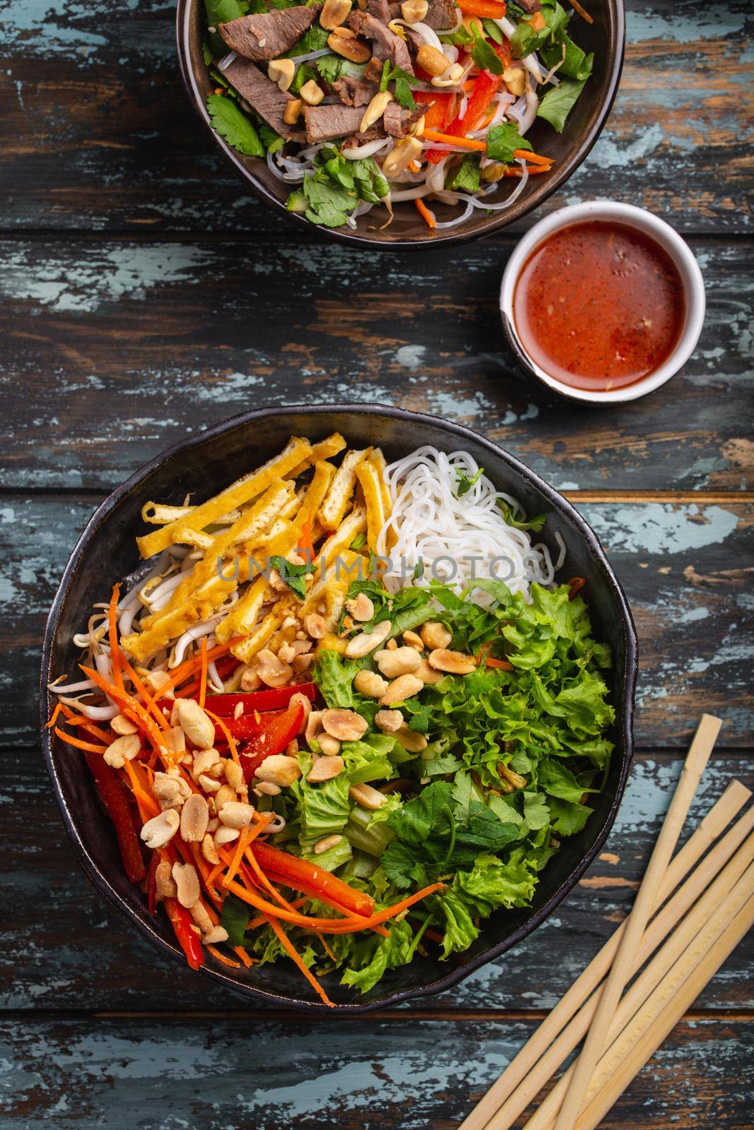 Asian, Chinese or Vietnamese style noodles salad with fresh vegetables, fried tofu and peanuts, served in rustic ceramic bowl on colorful wooden background. Healthy diet clean eating or vegan concept