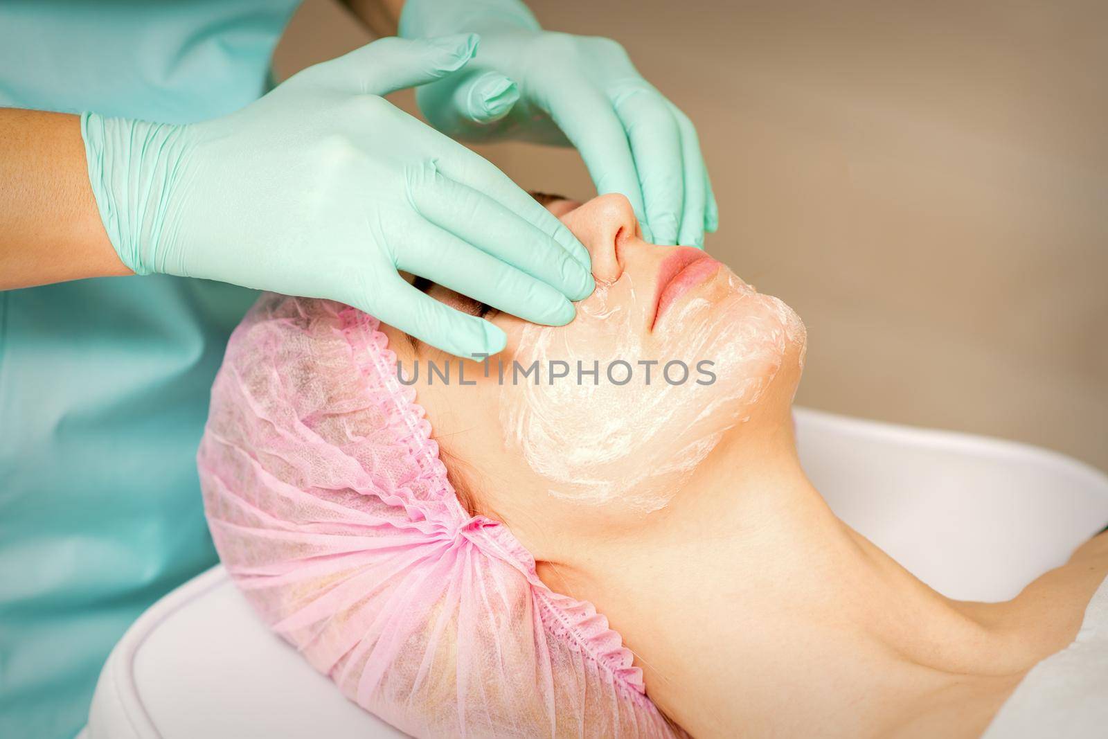 A cosmetologist is applying cream on the female face, close-up view. Woman with doctor beautician in beauty clinic