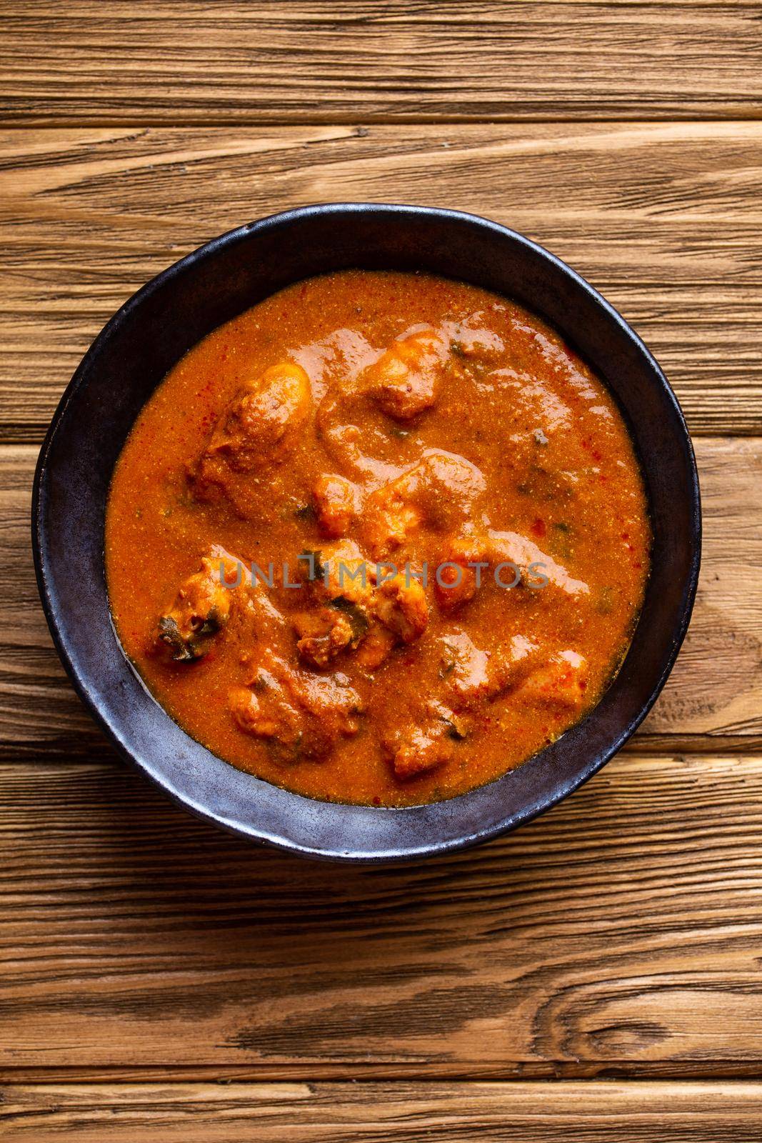 Indian chicken curry with tomato gravy on wooden rustic background. Traditional Indian dish butter chicken tikka masala, healthy lunch or dinner. Top view.