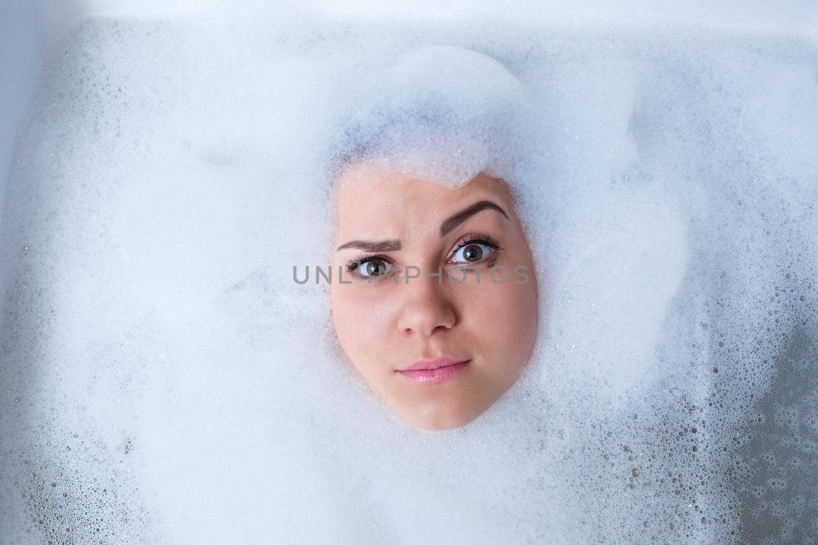 Closeup portrait of a girl in a bathtub and white foam around her face. Different emotions, grimaces, woman smile