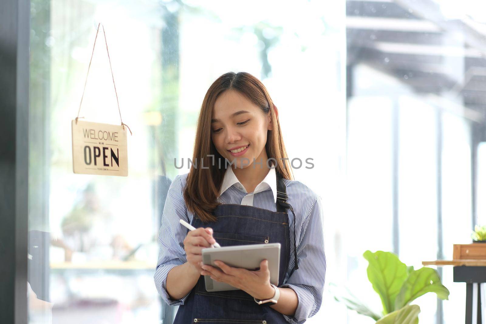 Startup successful small business owner sme beauty girl stand with tablet smartphone in coffee shop restaurant. Portrait of asian tan woman barista cafe owner. SME entrepreneur seller business concept by wichayada