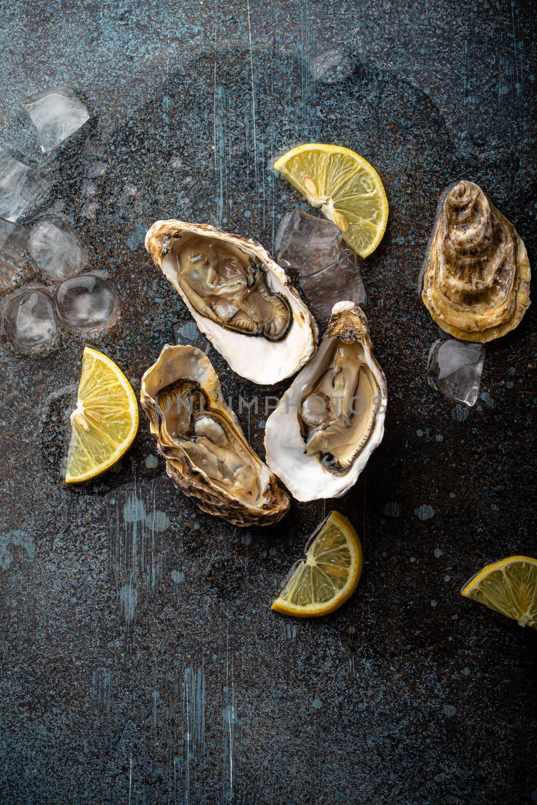 Fresh open oysters served with lemon wedges and ice cubes on rustic stone background top view, seafood oyster bar concept .