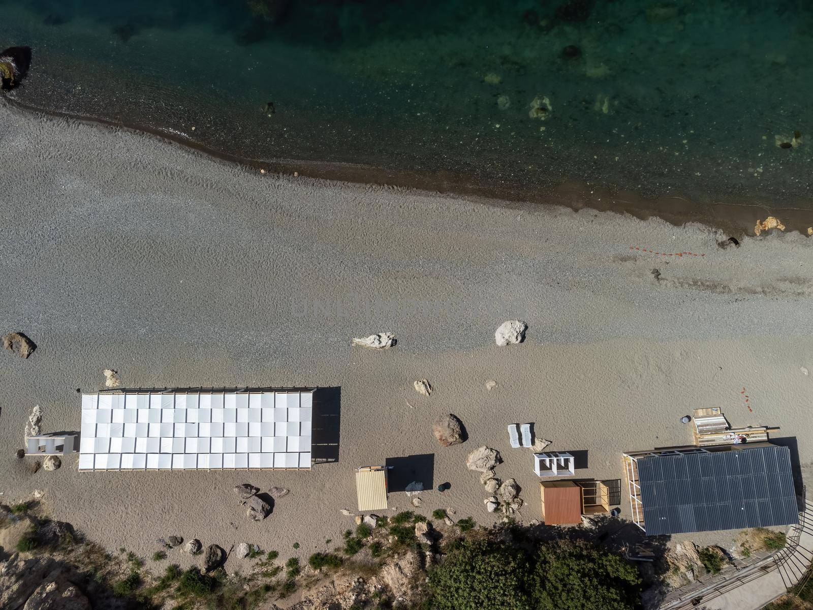 Empty sun loungers under a canopy on the beach. The beach area is empty. No people. White plastic sunbeds under the sun shade. The holiday season ends. Holiday season begins. Waiting for tourists