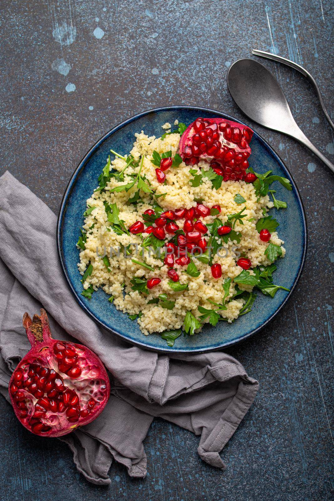 Bright colourful couscous or bulgur salad with pomegranate seeds Tabbouleh in rustic blue ceramic bowl top view on concrete background, traditional middle eastern or arab dish.