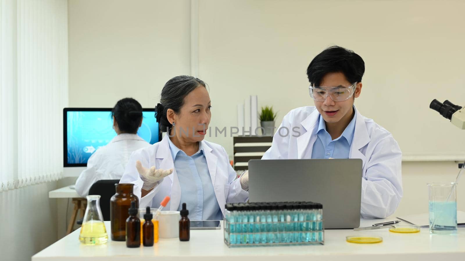 Senior female scientist and young male laboratory assistant analyzing and summarising information for scientific report.