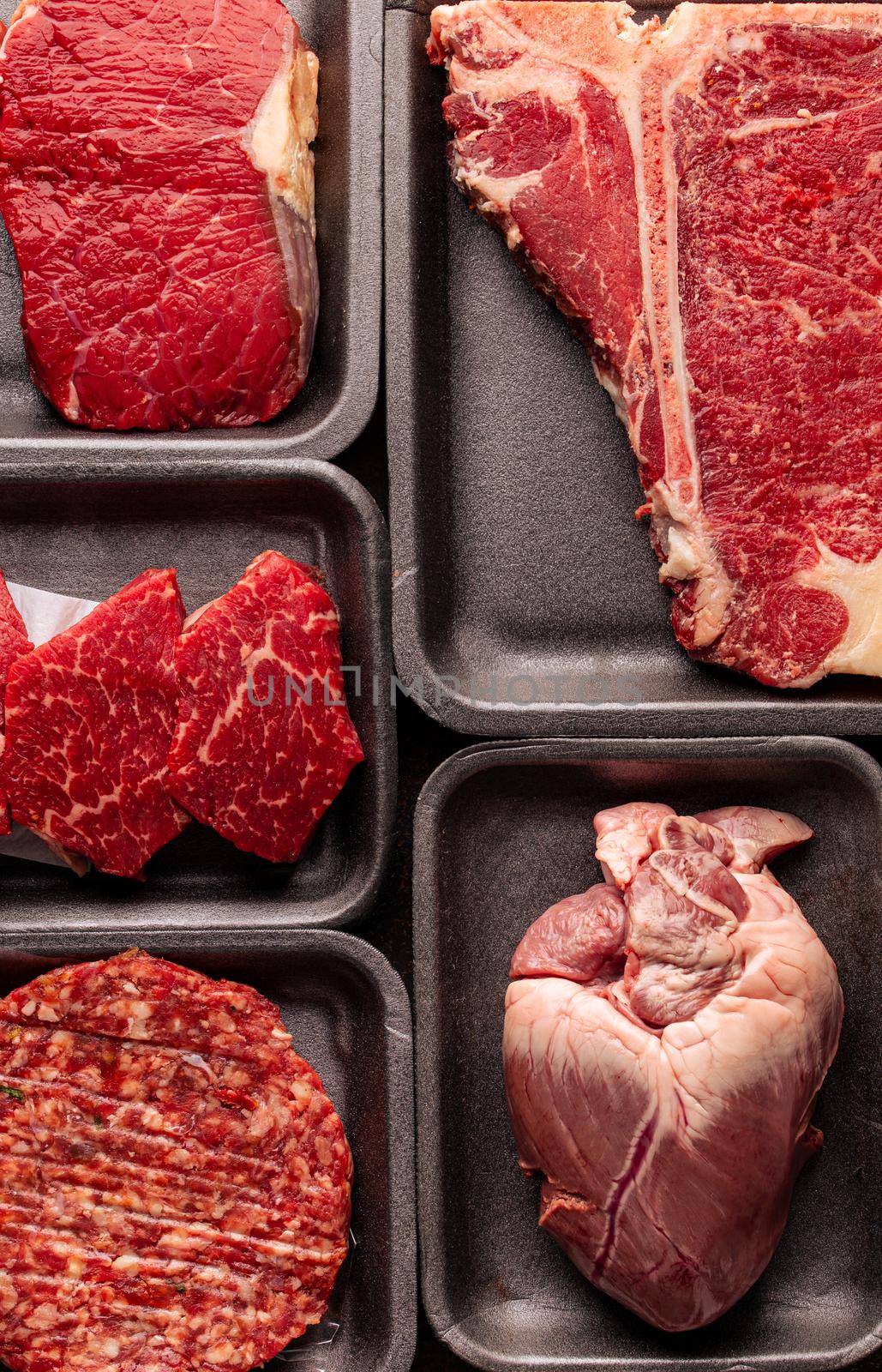 Black plastic packaging trays from supermarket with different types of fresh raw meat cuts, fresh beefbeef steaks and variety meats in boxes from above