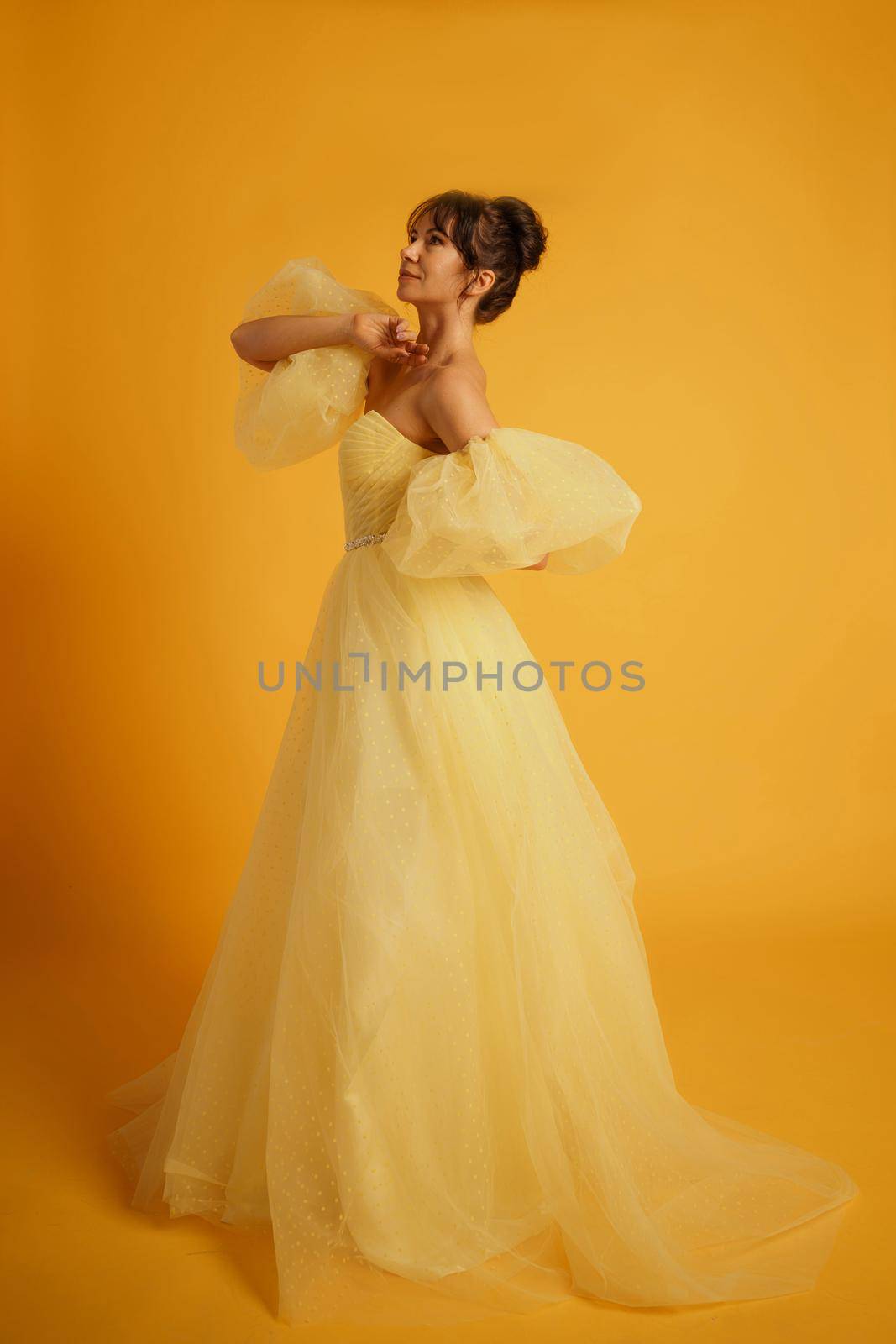 Portrait of a beautiful middle-aged woman in a yellow dress, her hair pulled up against a yellow background by Matiunina