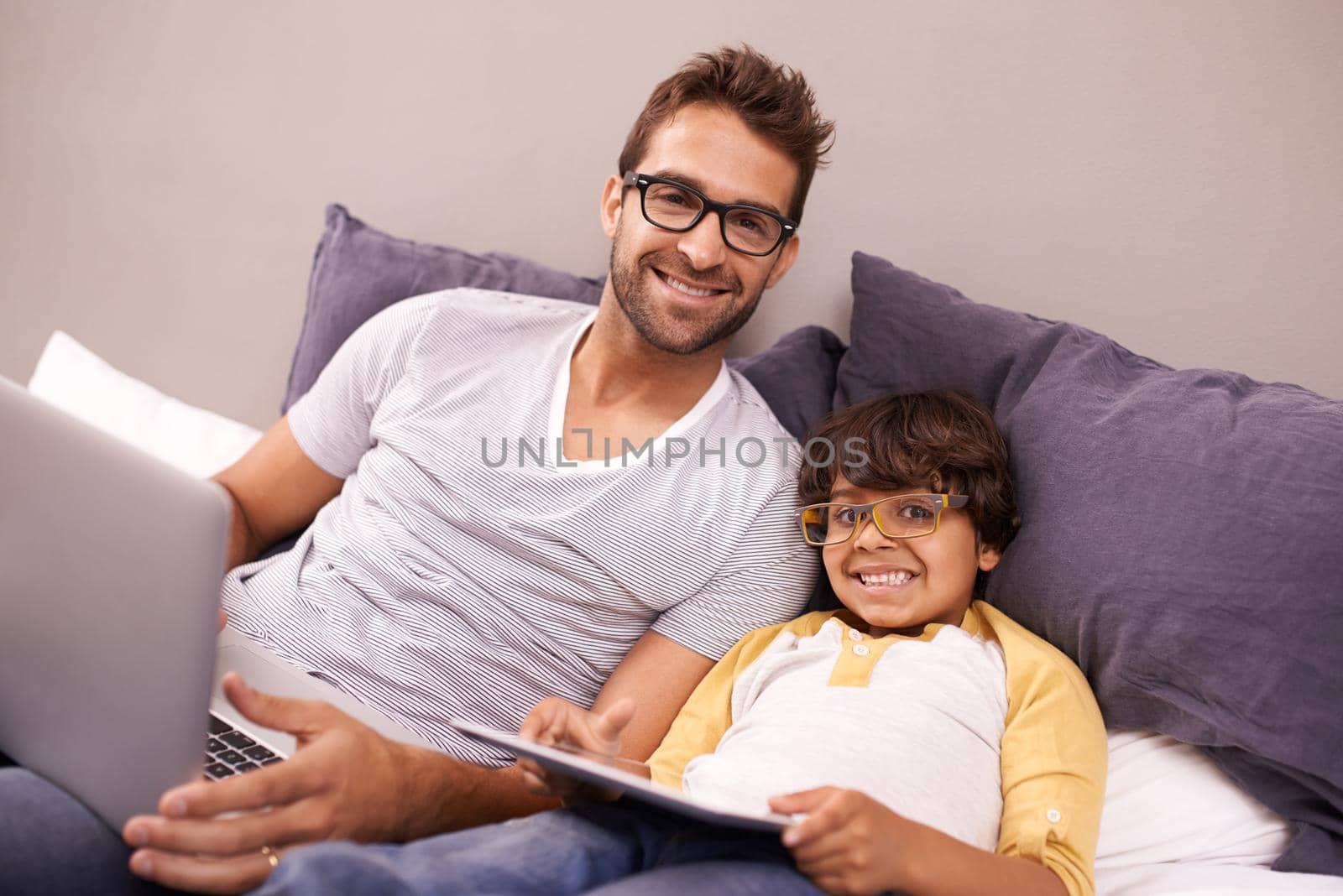 Technology is the best entertainment. Father and son lying on bed while using a laptop and a digital tablet