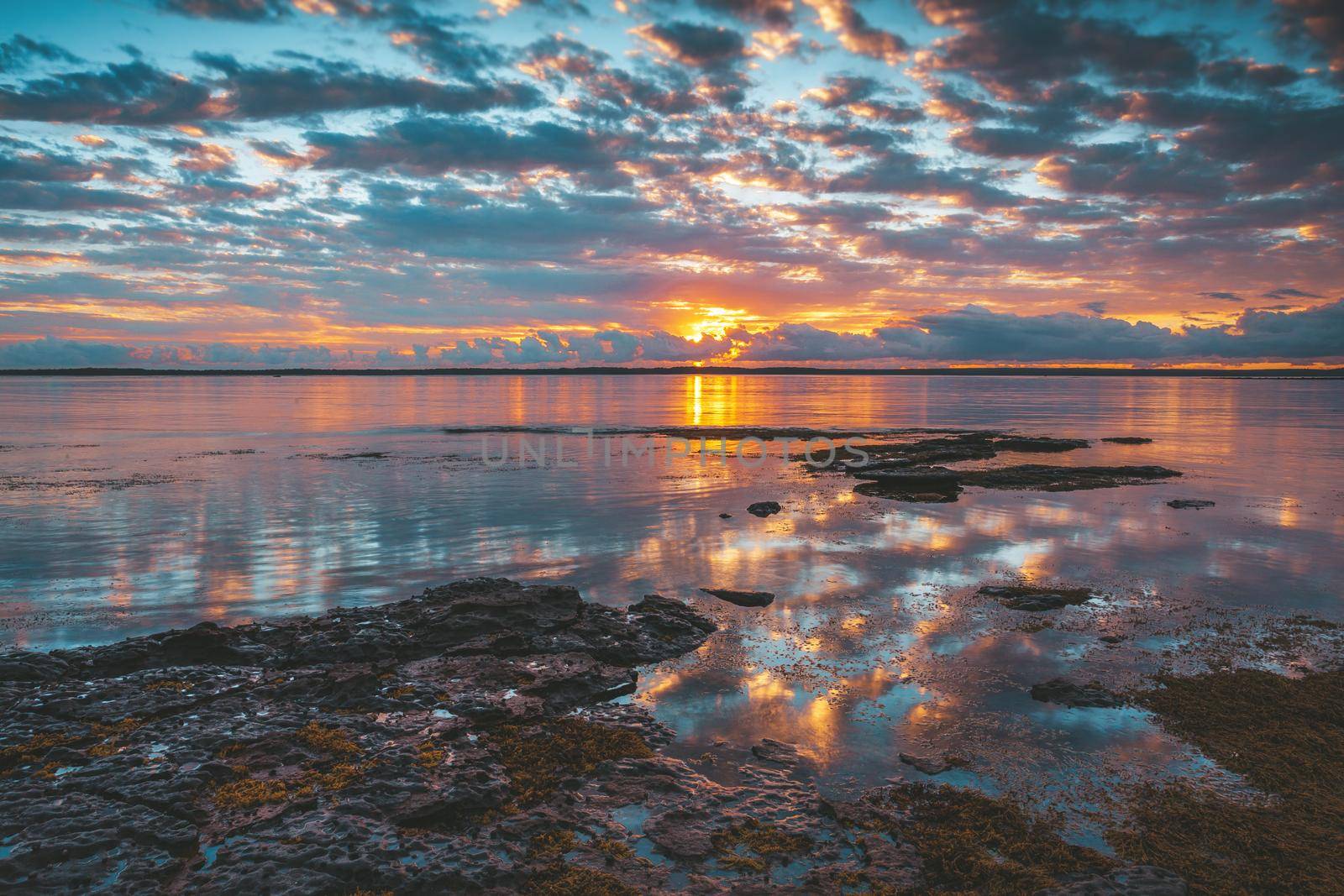 Tranquil waters and reflections of Jervis Bay.  A golden orange sun lights up the clouds