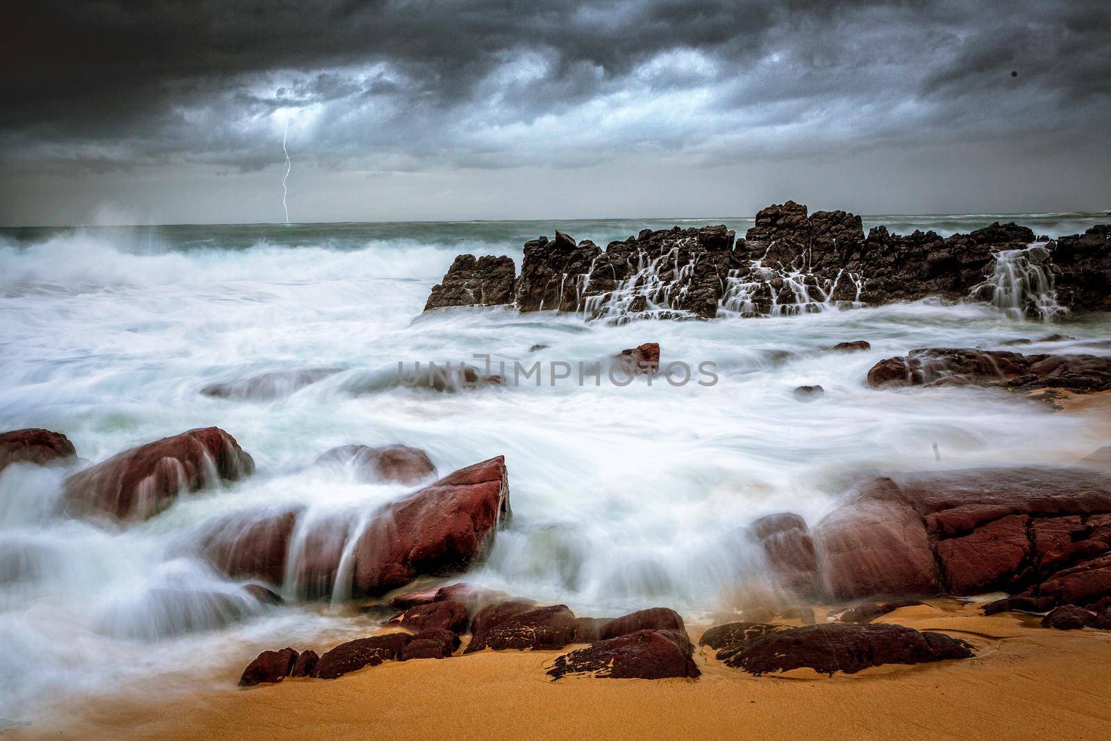 Storm over beach and turbulent waves crash over rocks onto seashore