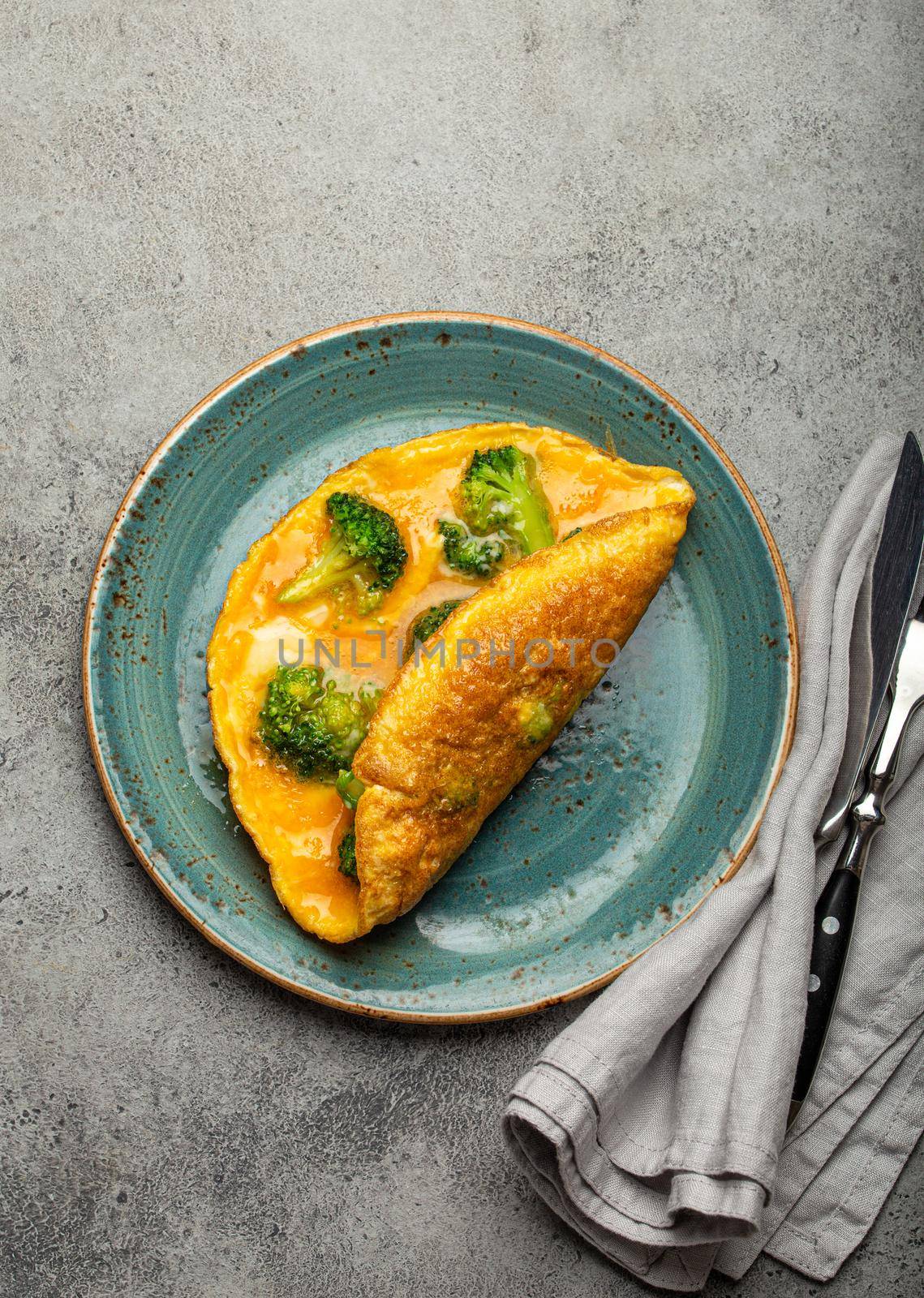 Healthy vegetarian egg omelette with green broccoli folded in half served on plate with fork and knife top view on gray stone concrete background table, diet and healthy clean eating concept