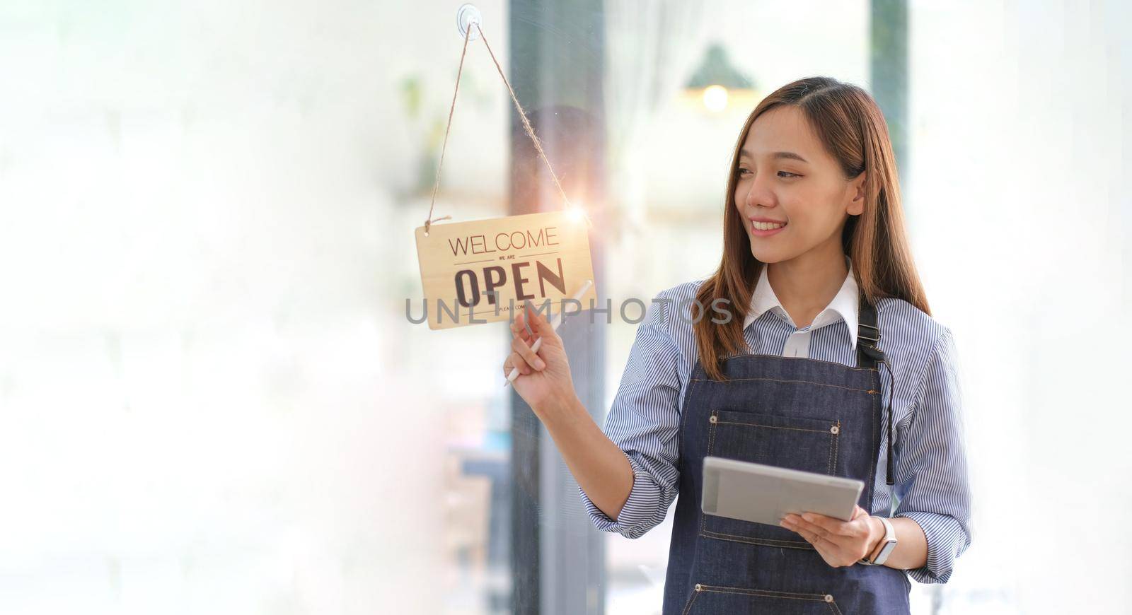 Startup successful small business owner sme beauty girl stand with tablet smartphone in coffee shop restaurant. Portrait of asian tan woman barista cafe owner. SME entrepreneur seller business concept by wichayada
