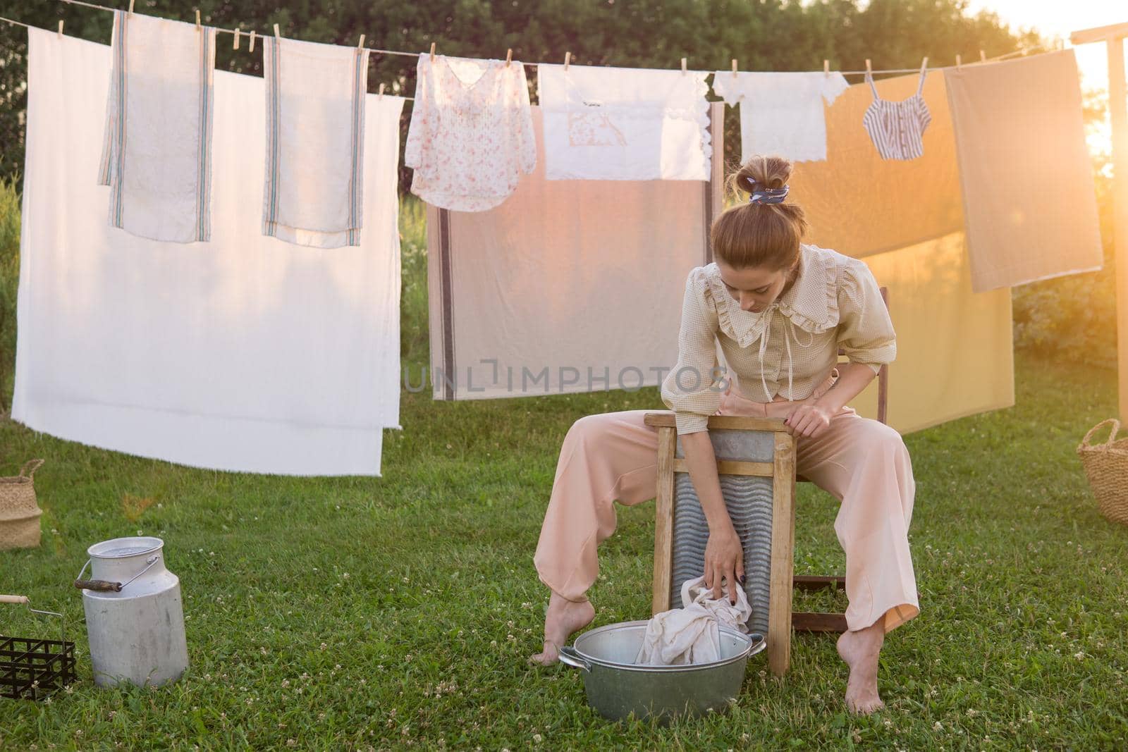 Laundry day. A woman hangs linen and towels on a tree in the courtyard of a village house. Summer cottage concept.