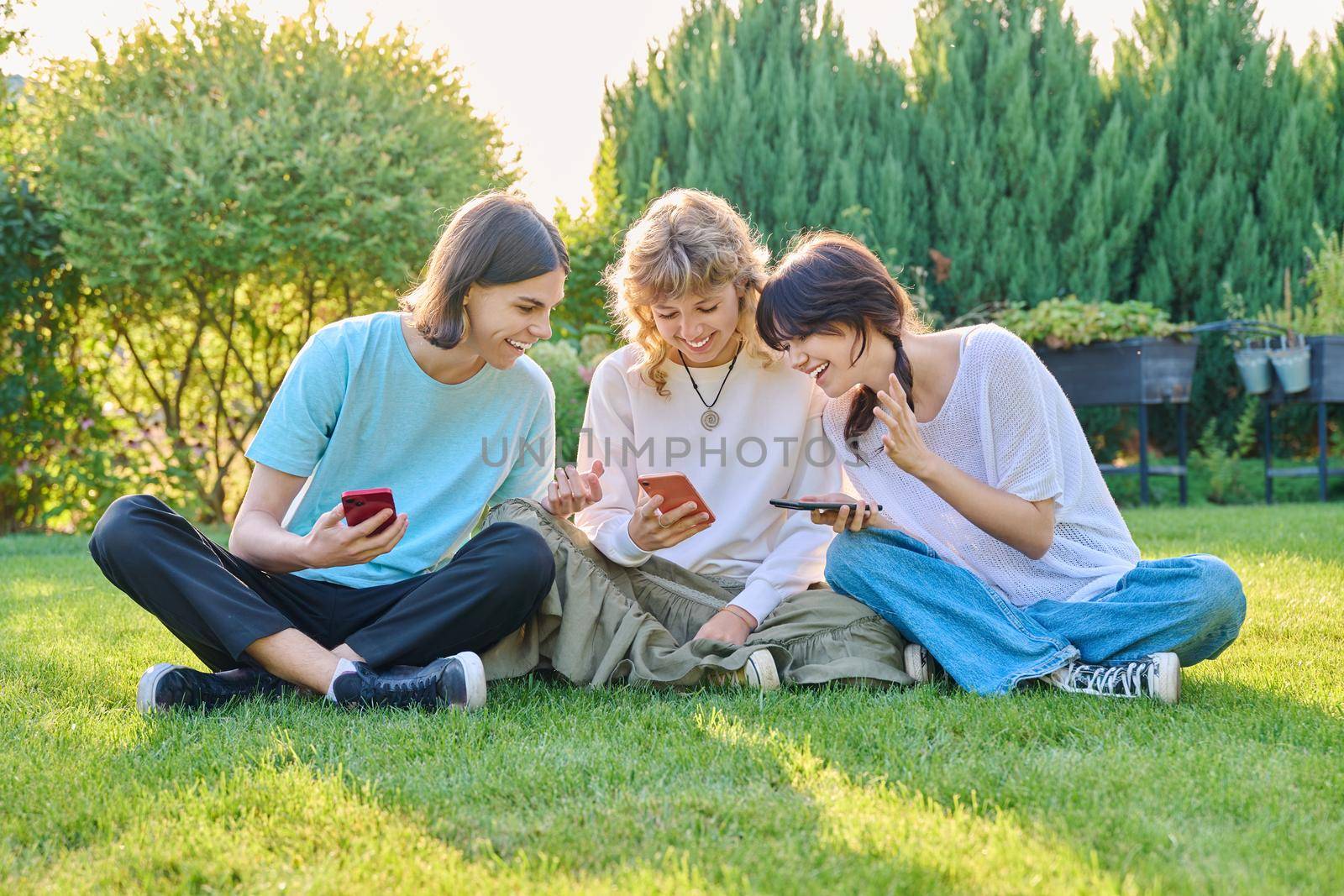 Teenage friends sitting on the grass with smartphones by VH-studio